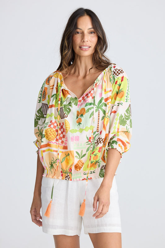 Woman wearing a colorful tropical print shirt and white shorts on a white background