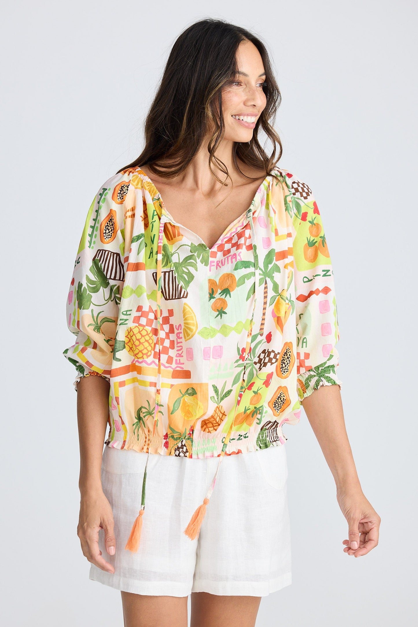 Woman wearing a colorful tropical print top and white shorts on a plain background