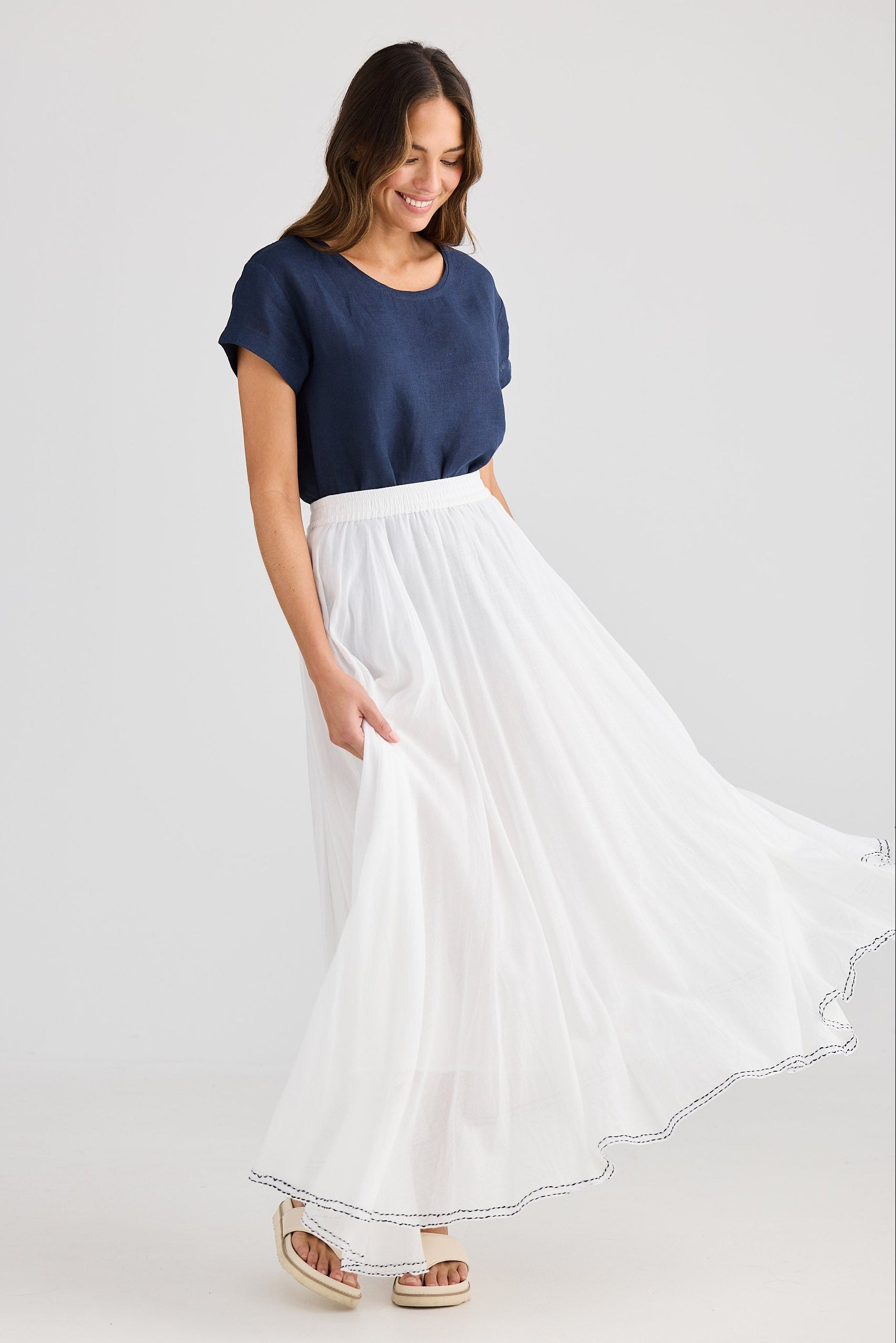 Woman wearing a navy top and white skirt on a light gray background