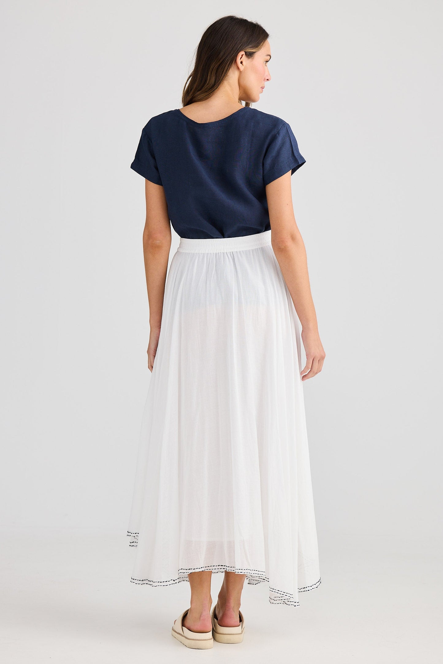 Woman wearing a navy top and white skirt on a light gray background