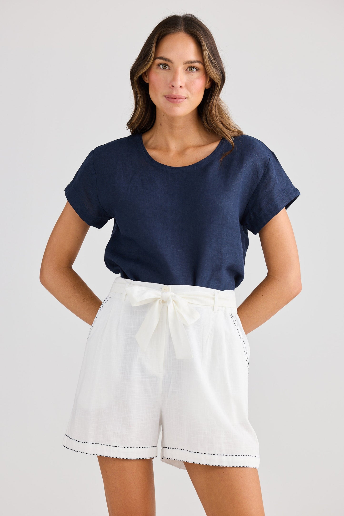 Woman wearing a navy blue top and white shorts on a plain background