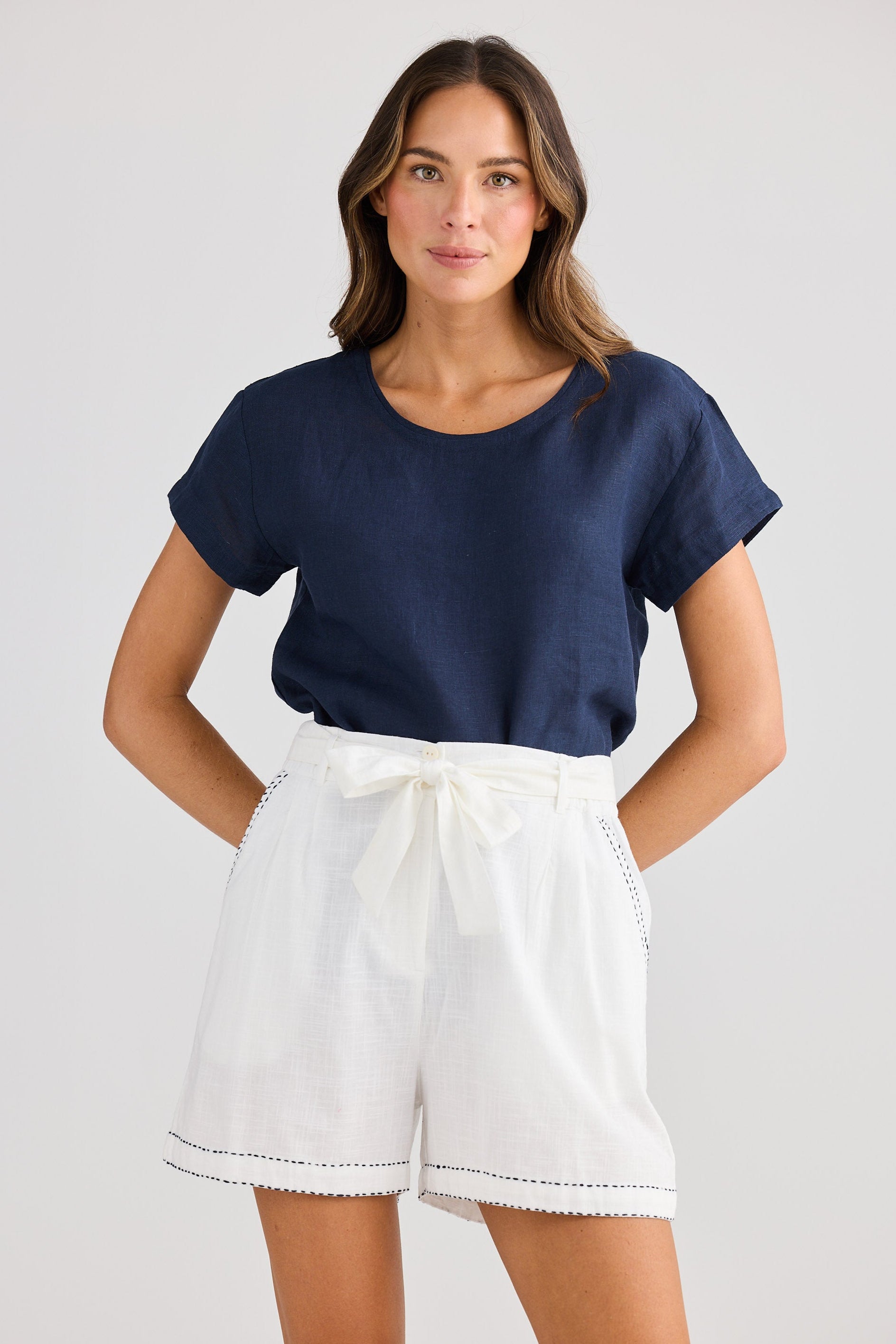 Woman wearing a navy blue top and white shorts on a plain background