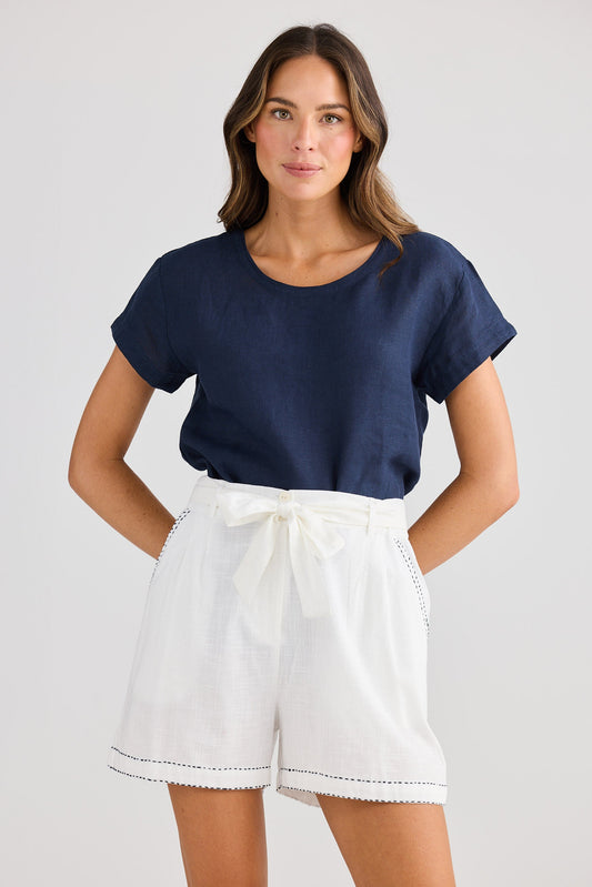Woman wearing a navy blue top and white shorts on a plain background