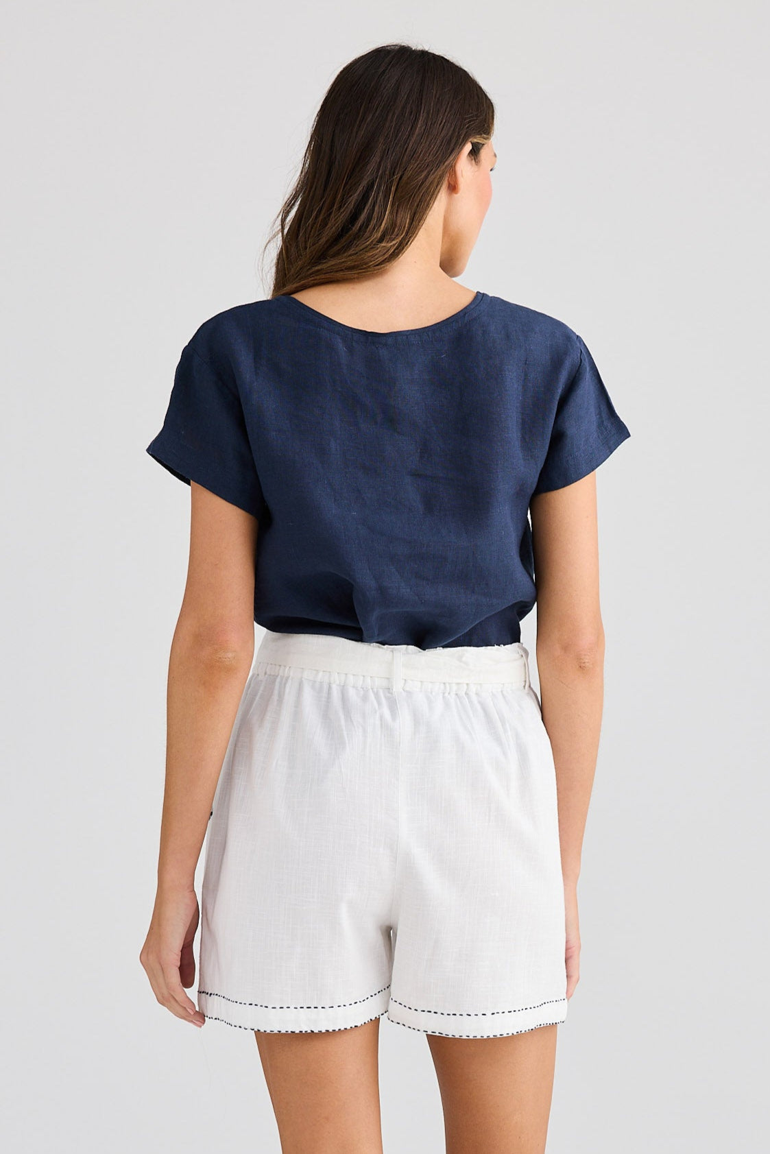 Person wearing a navy blue t-shirt and white shorts on a plain background