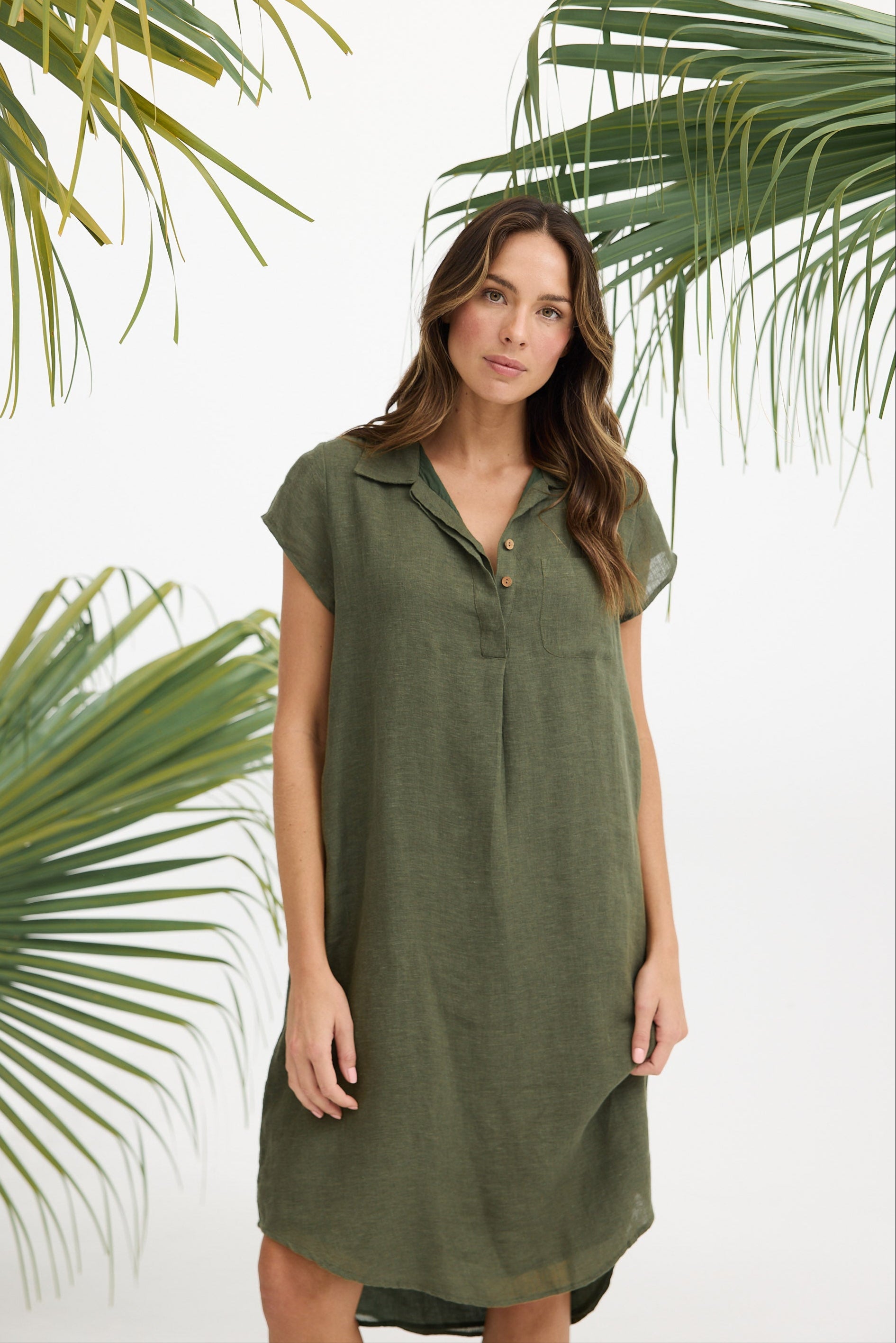 Woman wearing a green dress standing against a white background with palm leaves.