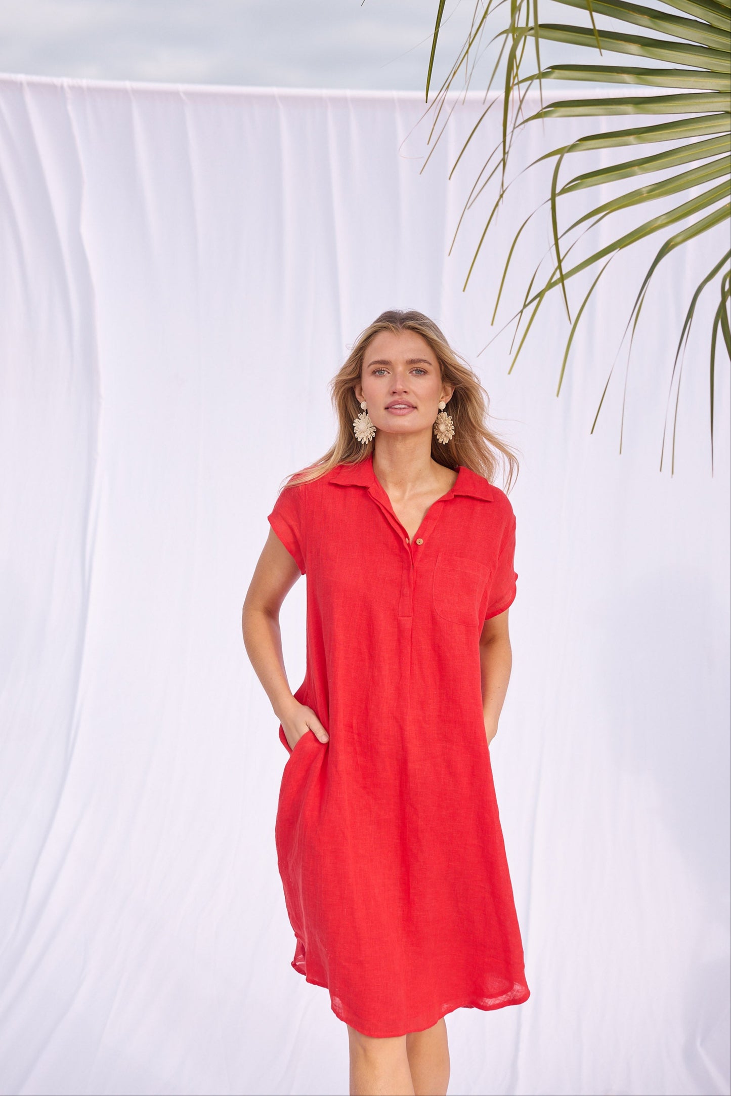Woman wearing a red dress standing against a white background with a palm leaf.