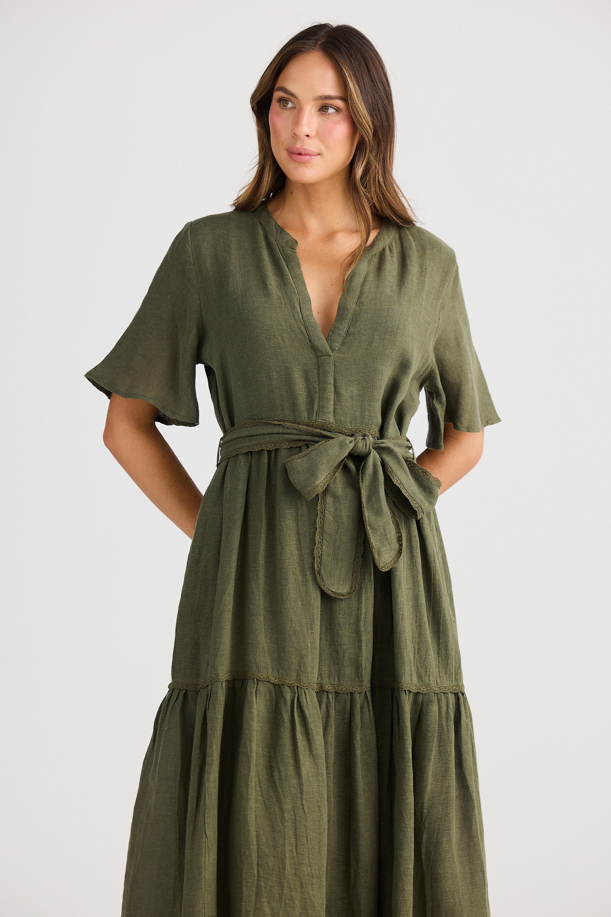 Woman wearing an olive green dress with a belt on a white background