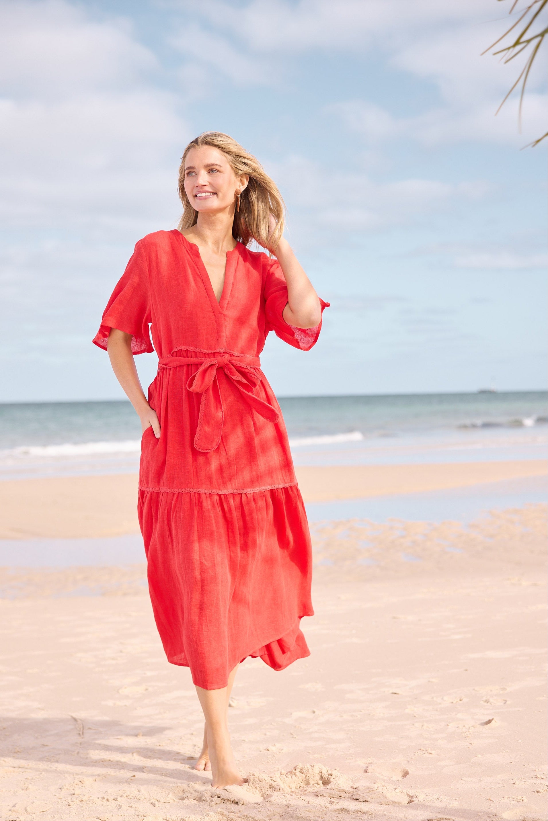 Woman in a red dress standing on a beach with blue sky and ocean in the background