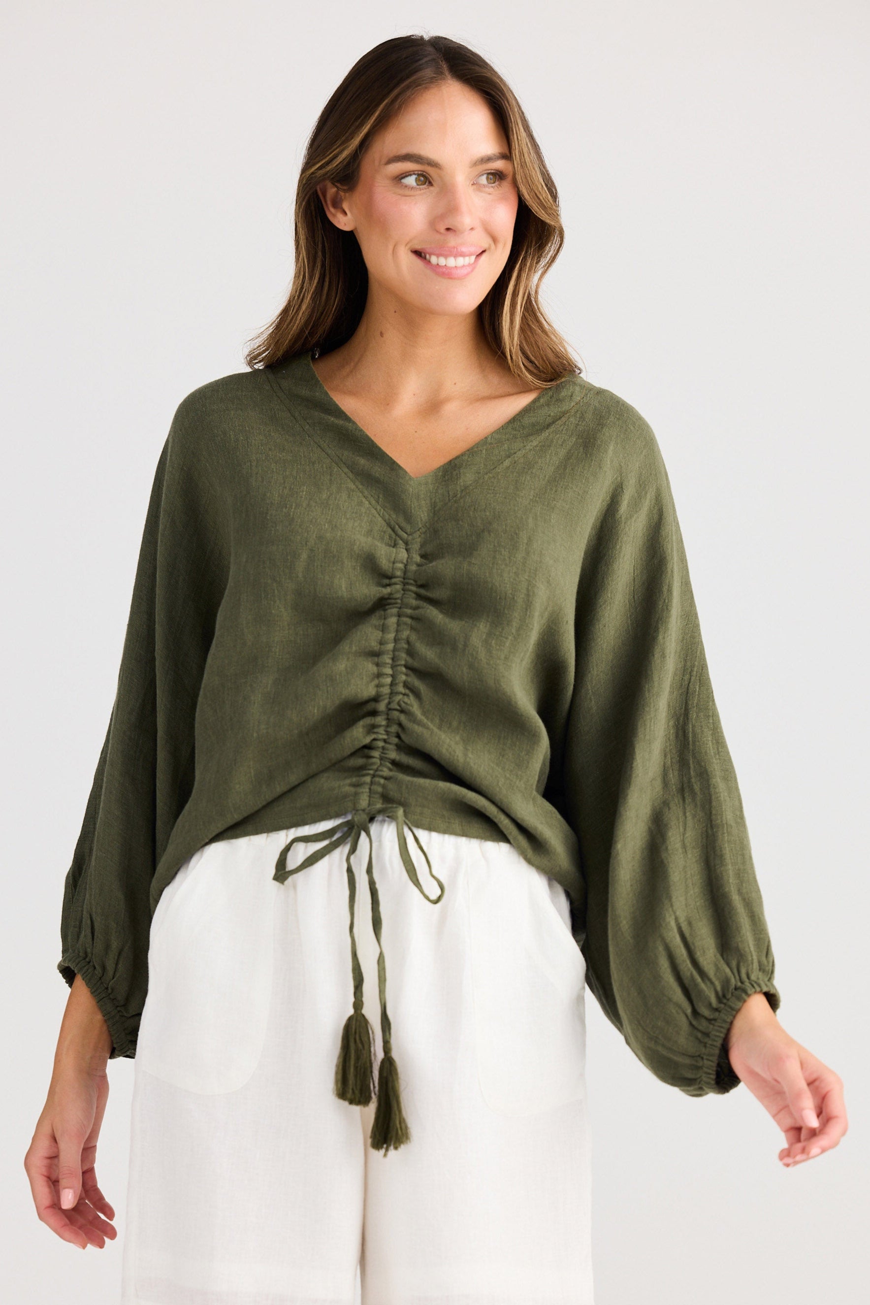 Woman wearing an olive green blouse and white shorts on a white background