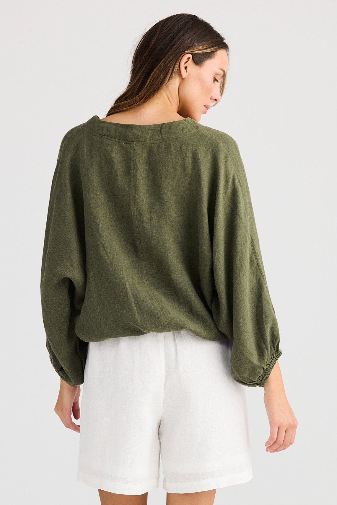 Woman wearing a green sweater and white shorts on a plain background