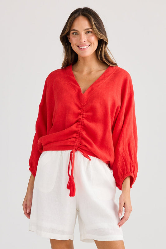 Woman wearing a red shirt and white shorts on a plain background