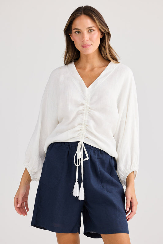 Woman wearing a white blouse and navy shorts on a plain background