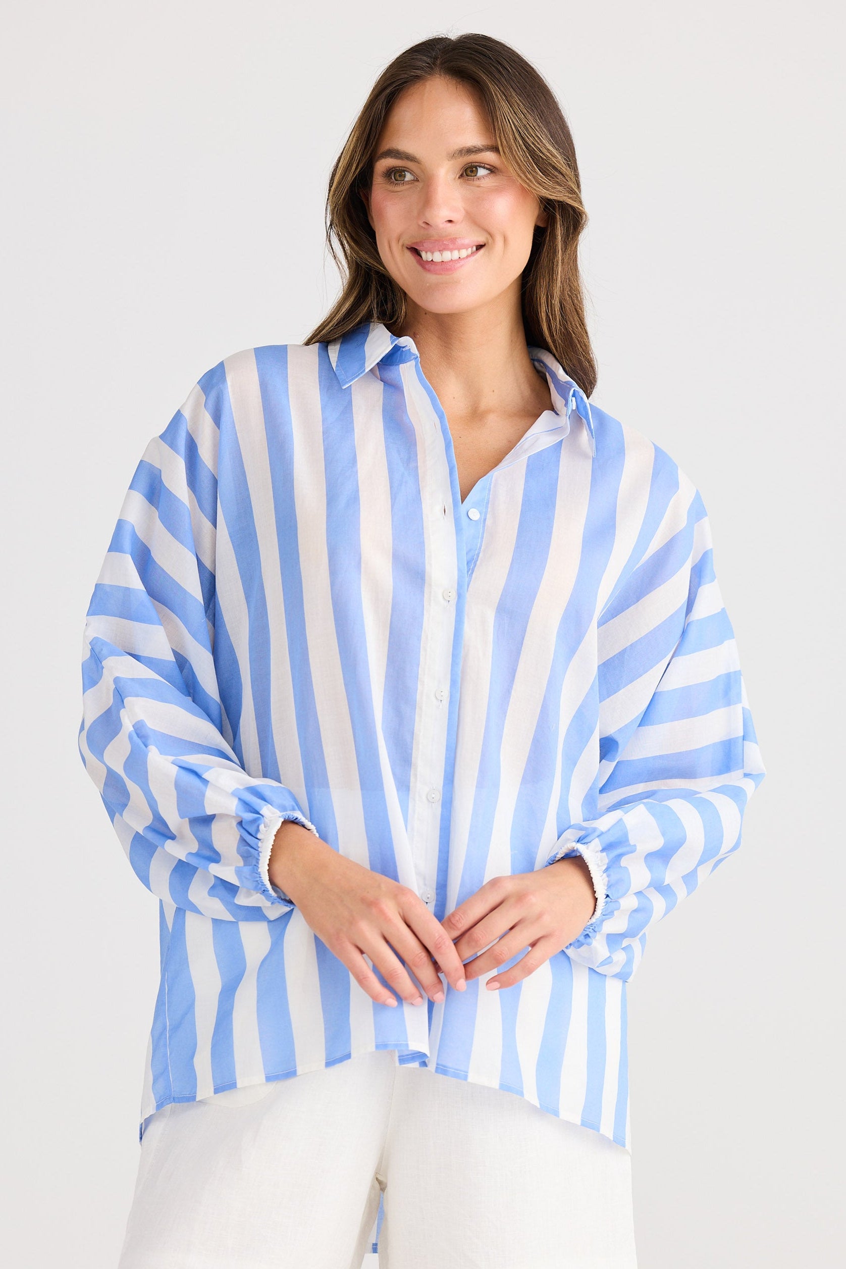 Woman wearing a blue and white striped shirt with white shorts on a white background