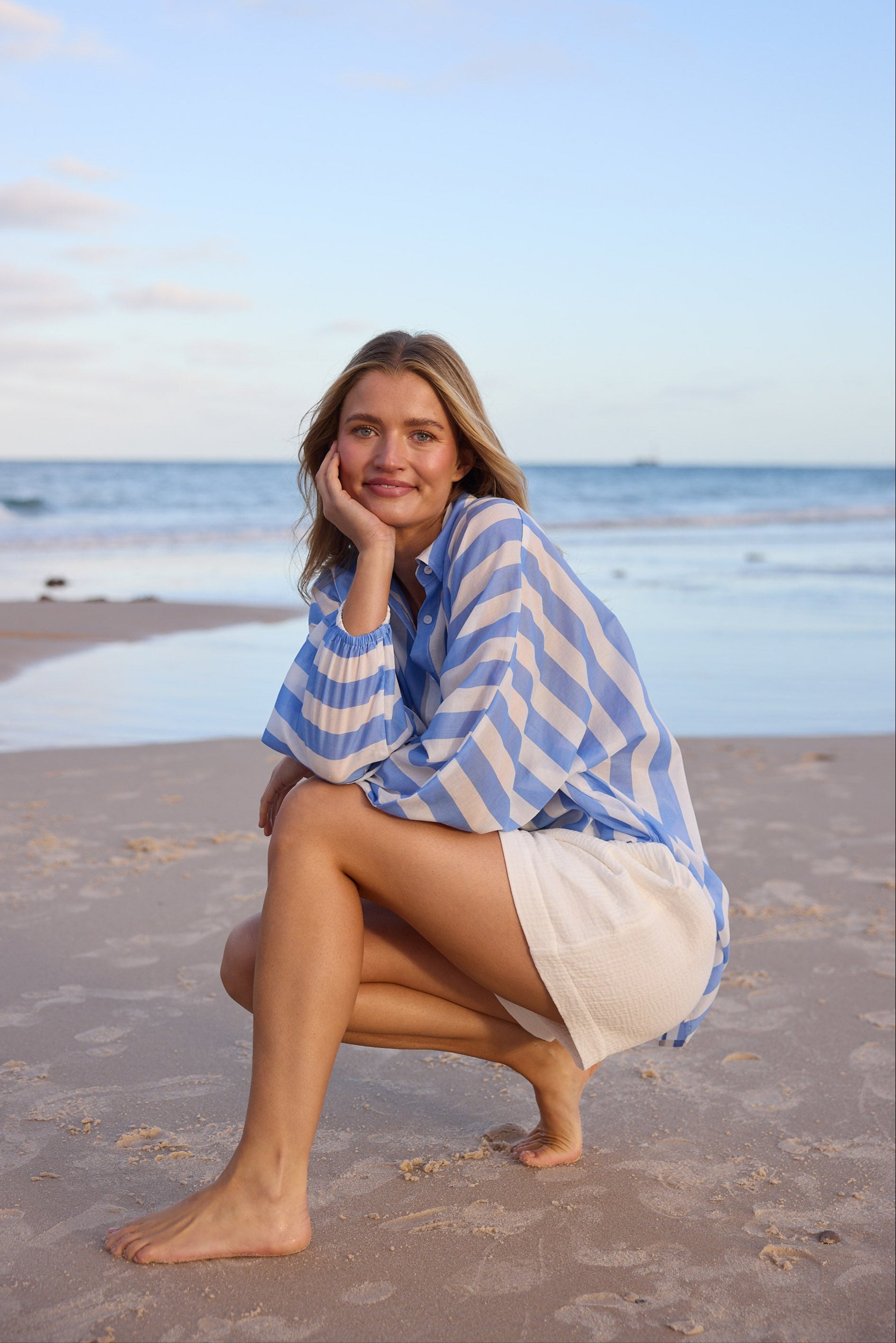 Woman in a blue and white striped cover-up sitting on the beach.