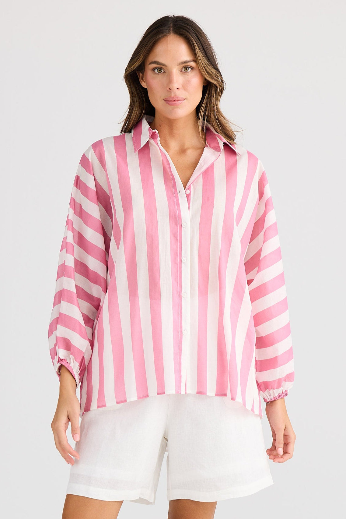 Woman wearing a pink and white striped shirt with white shorts on a white background