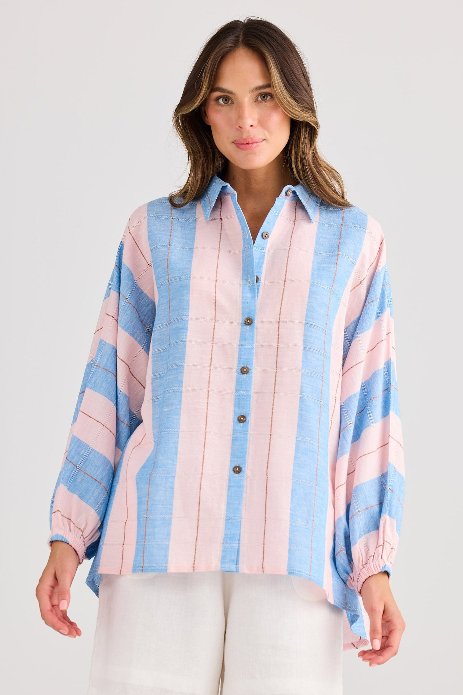 Woman wearing a colorful striped shirt and white shorts on a plain background