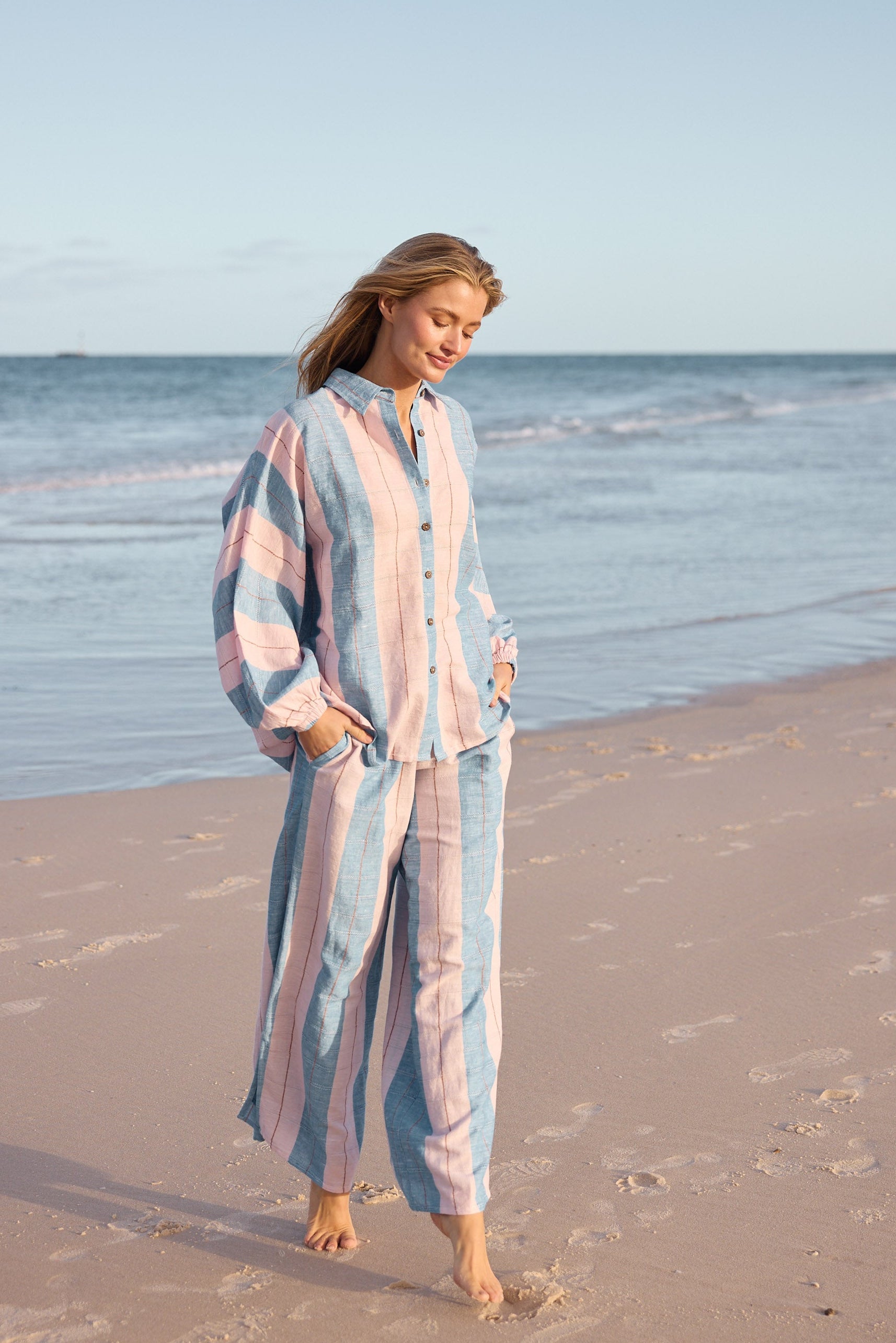 Woman in a striped outfit standing on a beach with ocean in the background