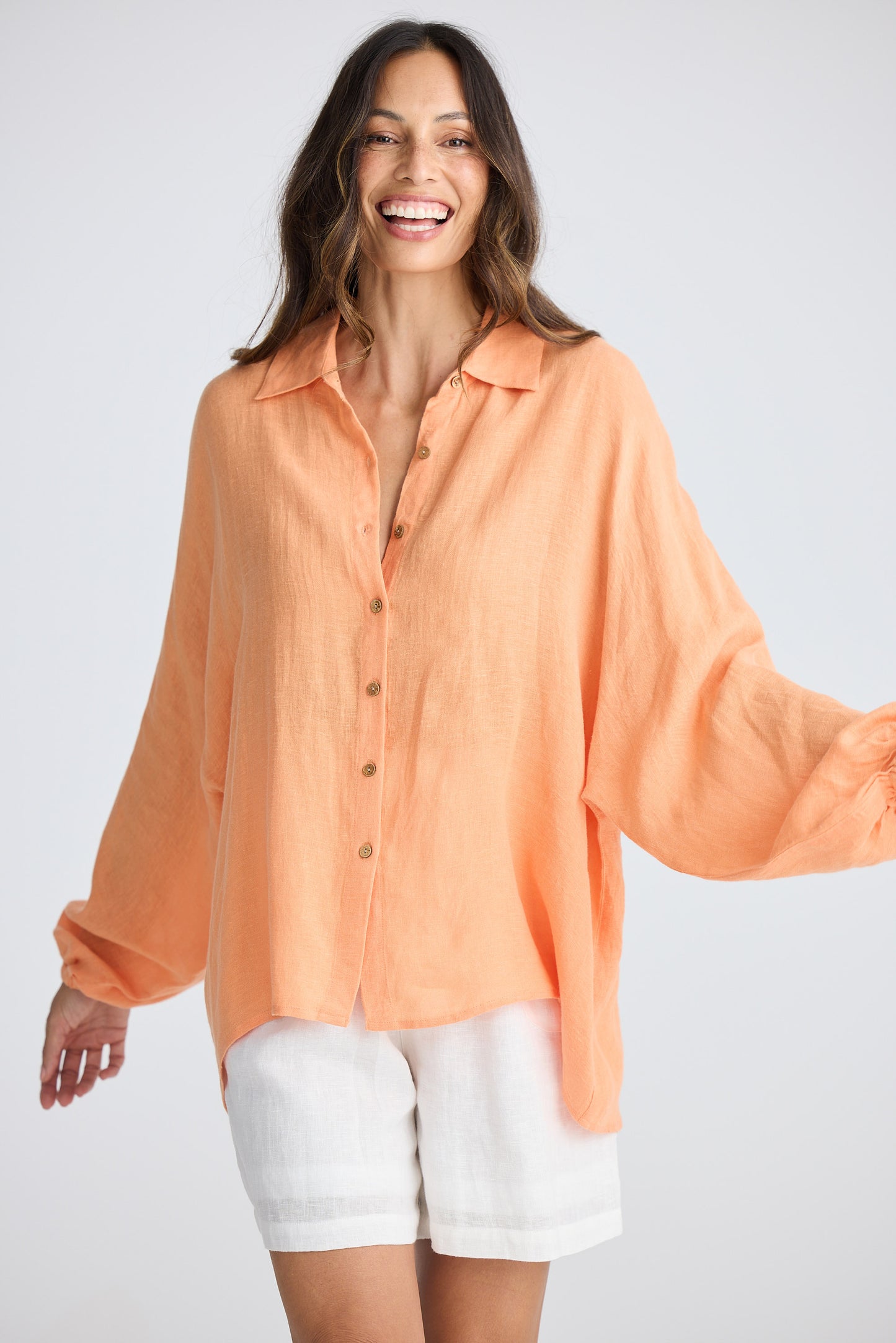 Woman wearing an orange blouse and white shorts on a plain background