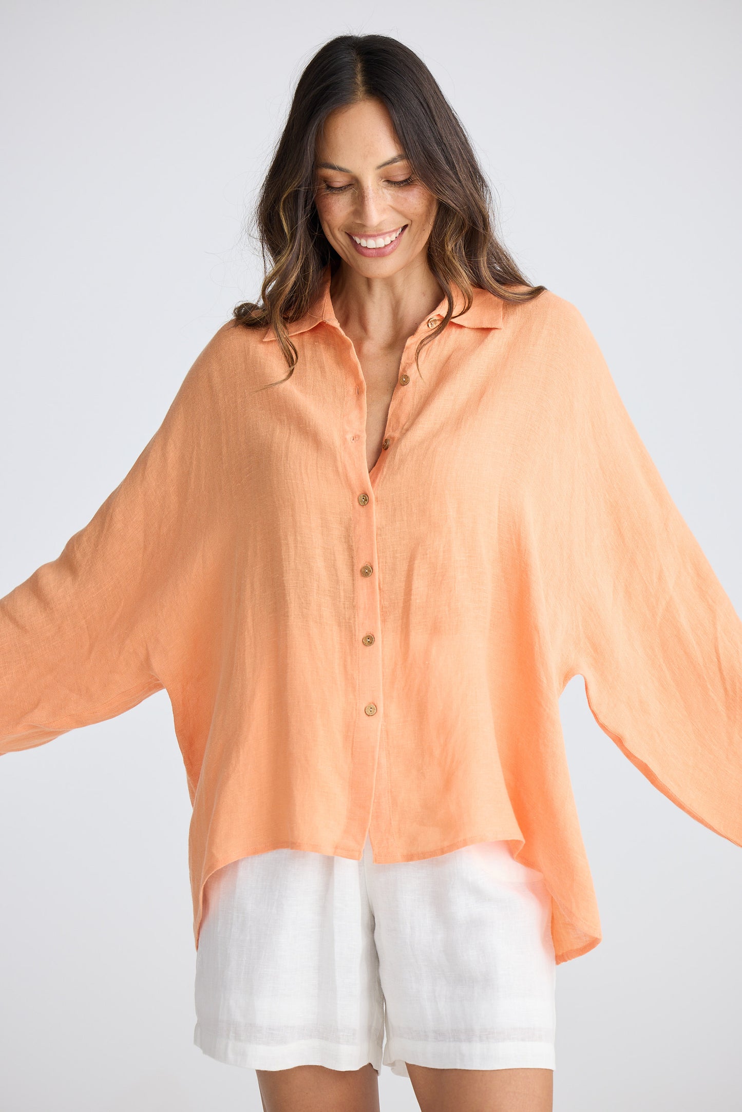 Woman wearing an orange blouse and white shorts on a plain background
