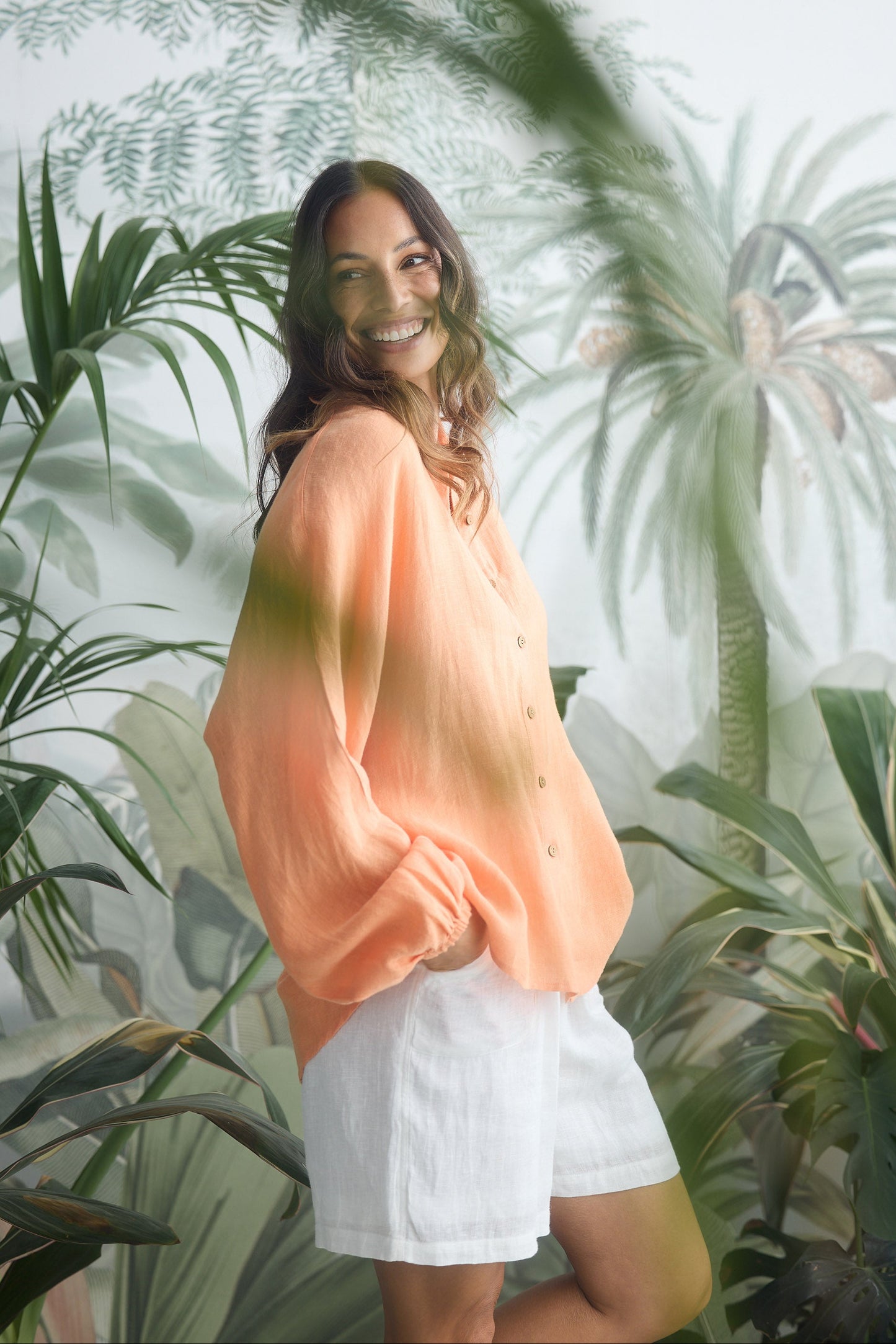 Woman in peach top and white shorts standing in front of a tropical plant background