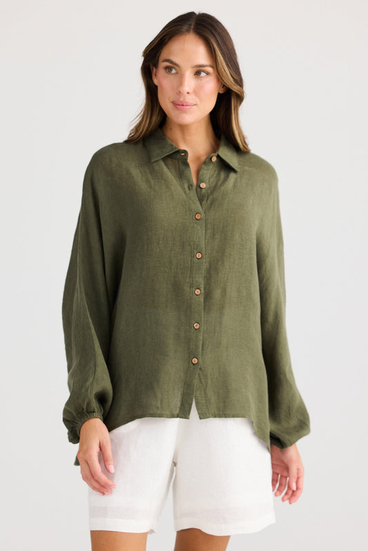 Woman wearing an olive green button-up shirt and white shorts on a light gray background