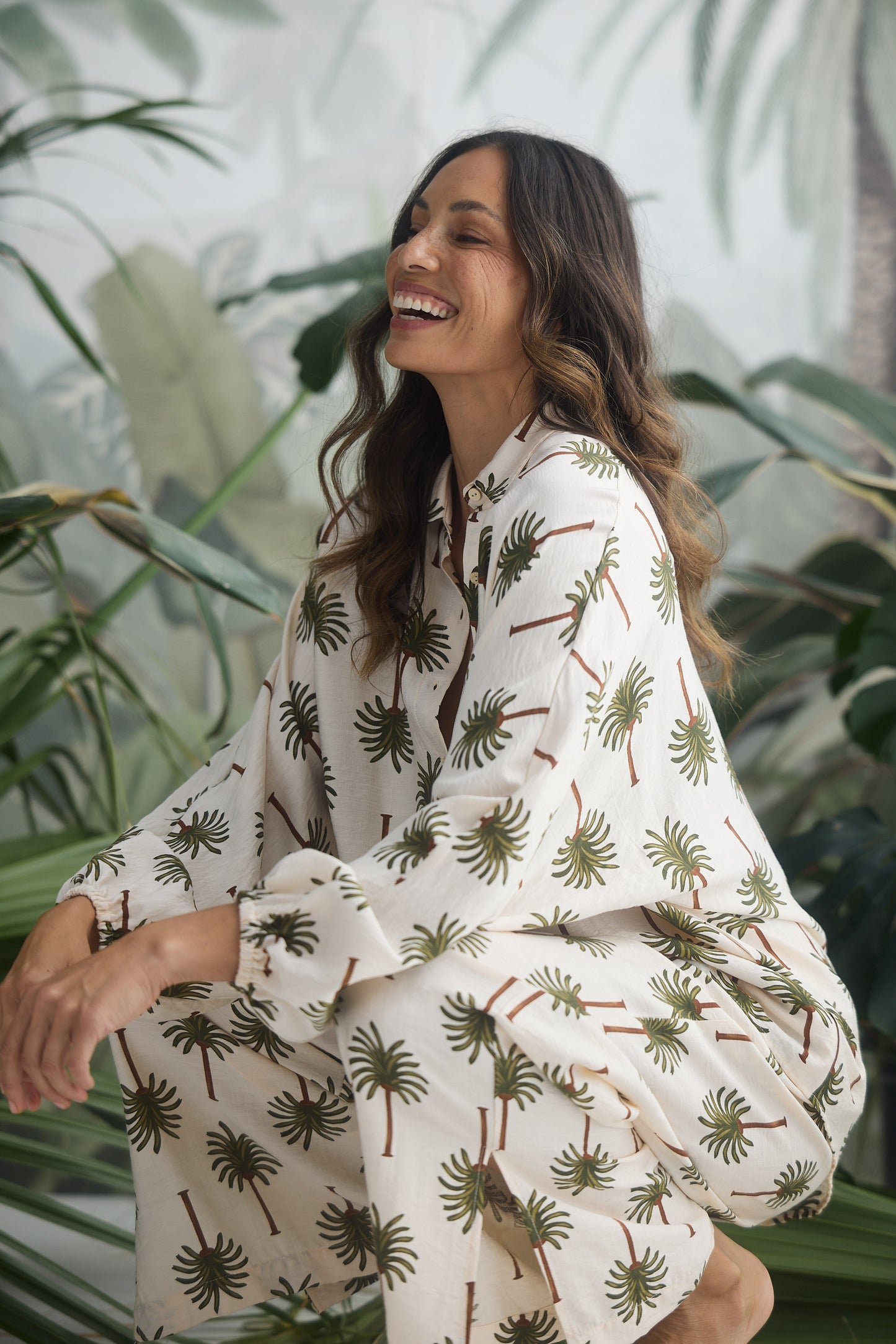 Woman wearing a white shirt and pants with green leaf pattern in a tropical setting
