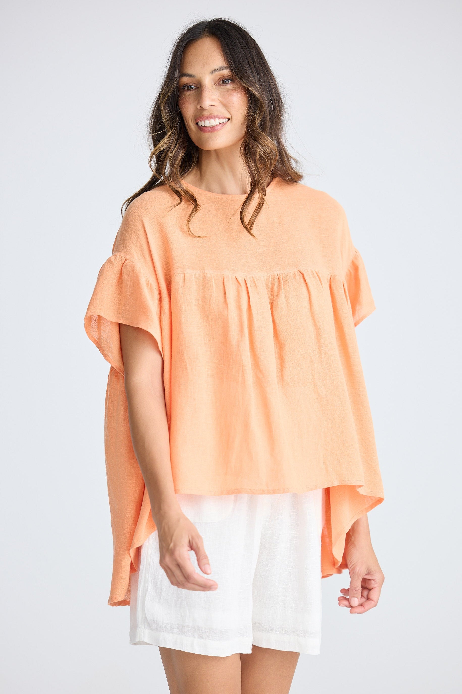 Woman wearing orange short sleeve top and white shorts on white background