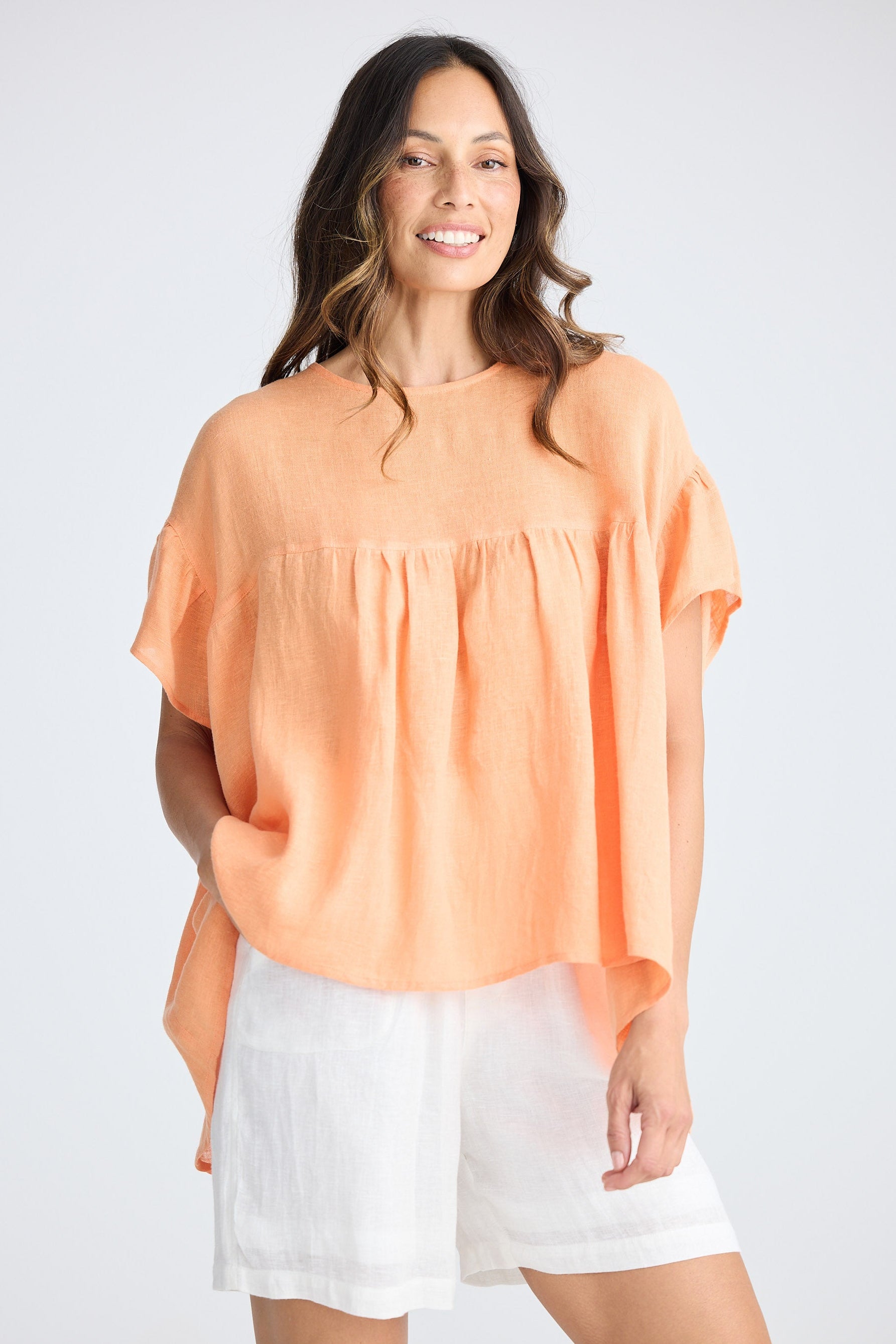 Woman wearing orange short sleeve top and white shorts on white background
