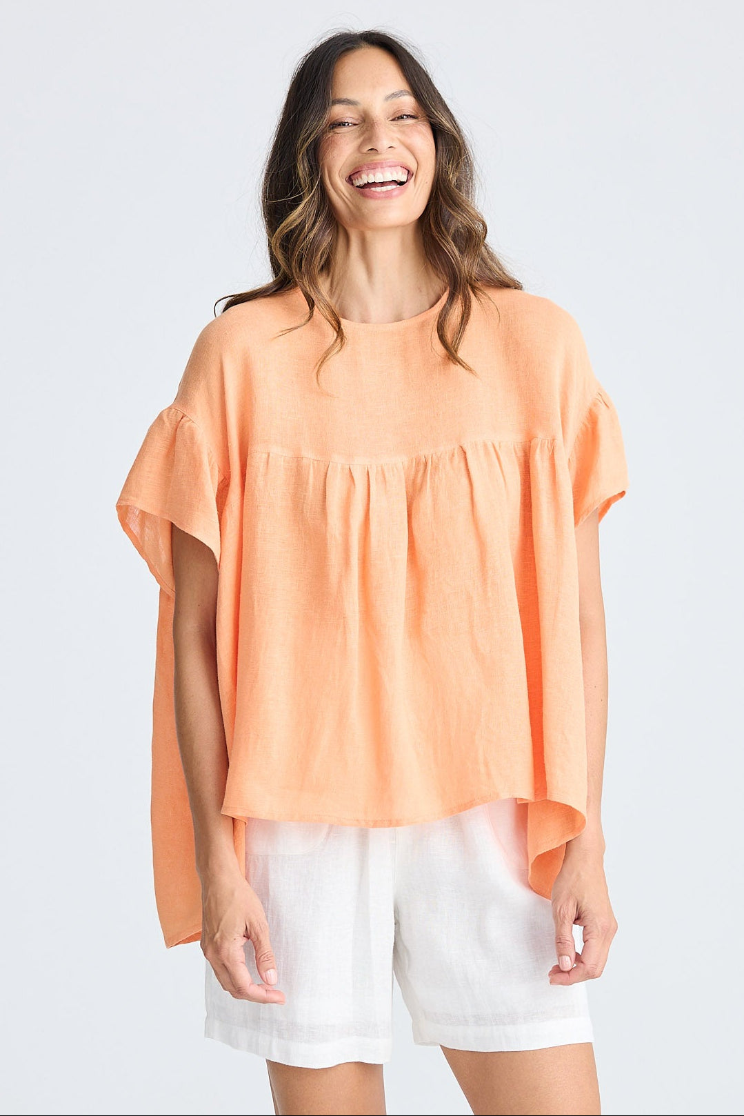 Woman wearing orange short sleeve top and white shorts on white background