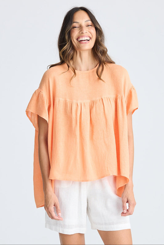 Woman wearing orange short sleeve top and white shorts on white background