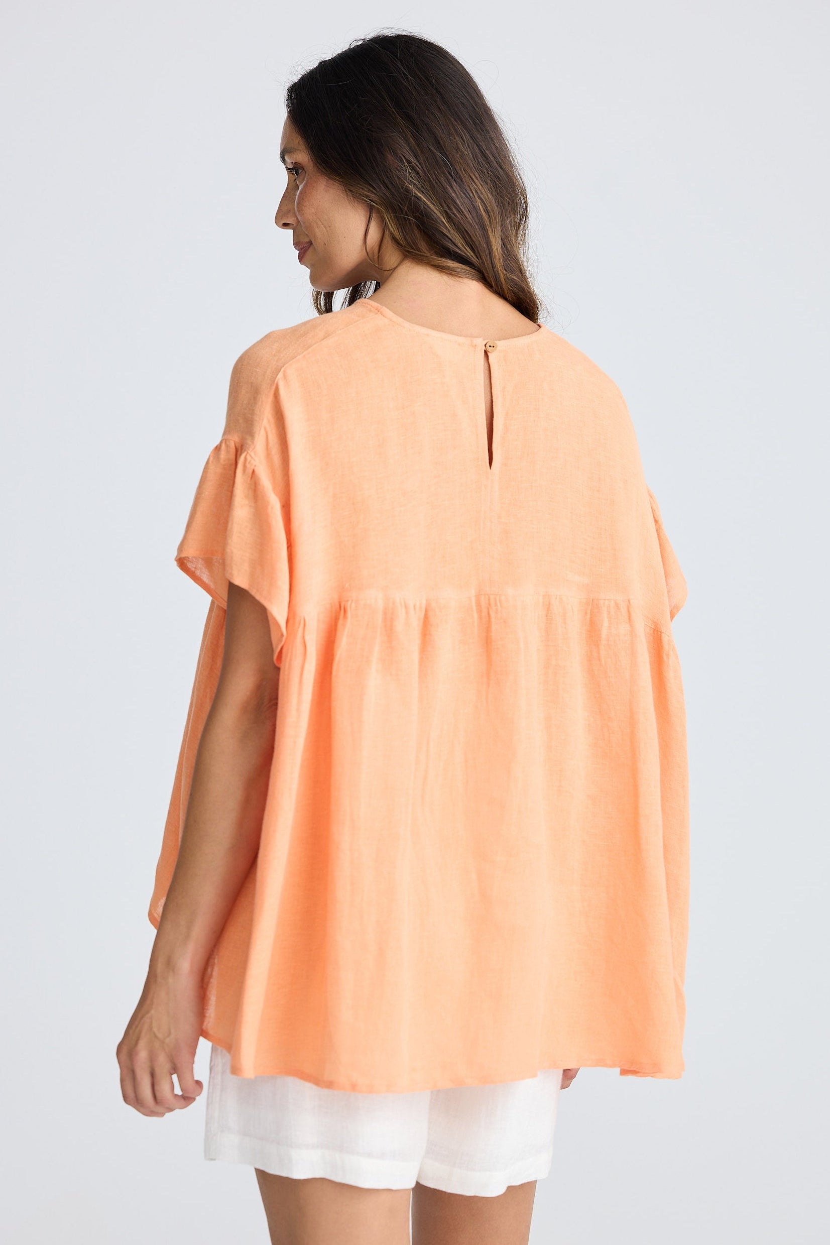 Woman wearing orange short sleeve top and white shorts on white background