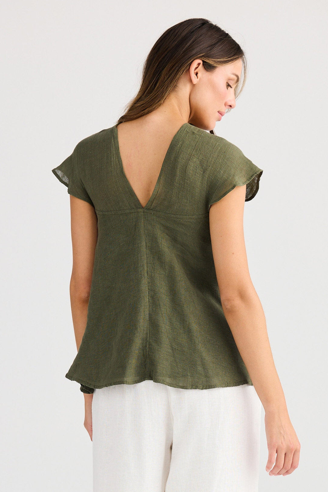 Woman wearing a green top and white pants on a plain background