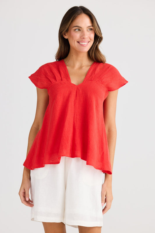 Woman wearing a red blouse and white pants on a plain background