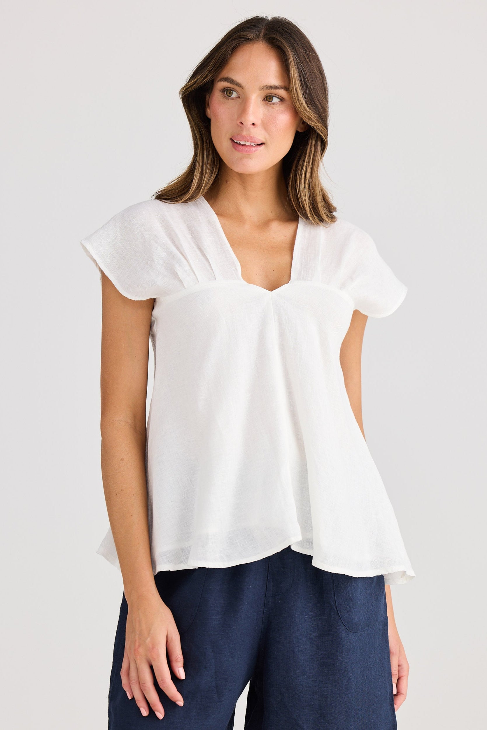 Woman wearing a white blouse and navy shorts on a plain background
