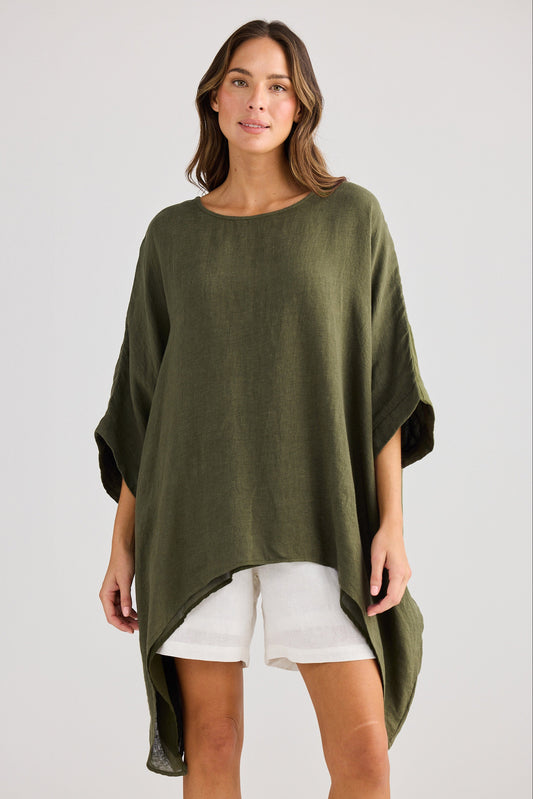 Woman wearing a green poncho over a white outfit on a plain background