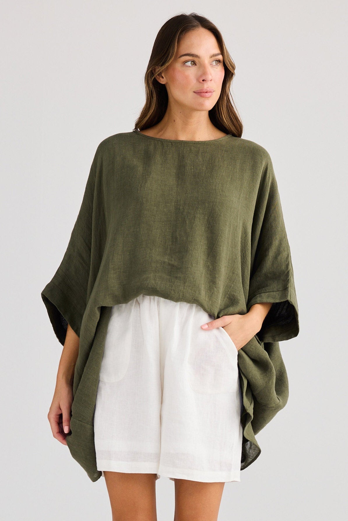 Woman wearing a green sweater and white shorts on a plain background