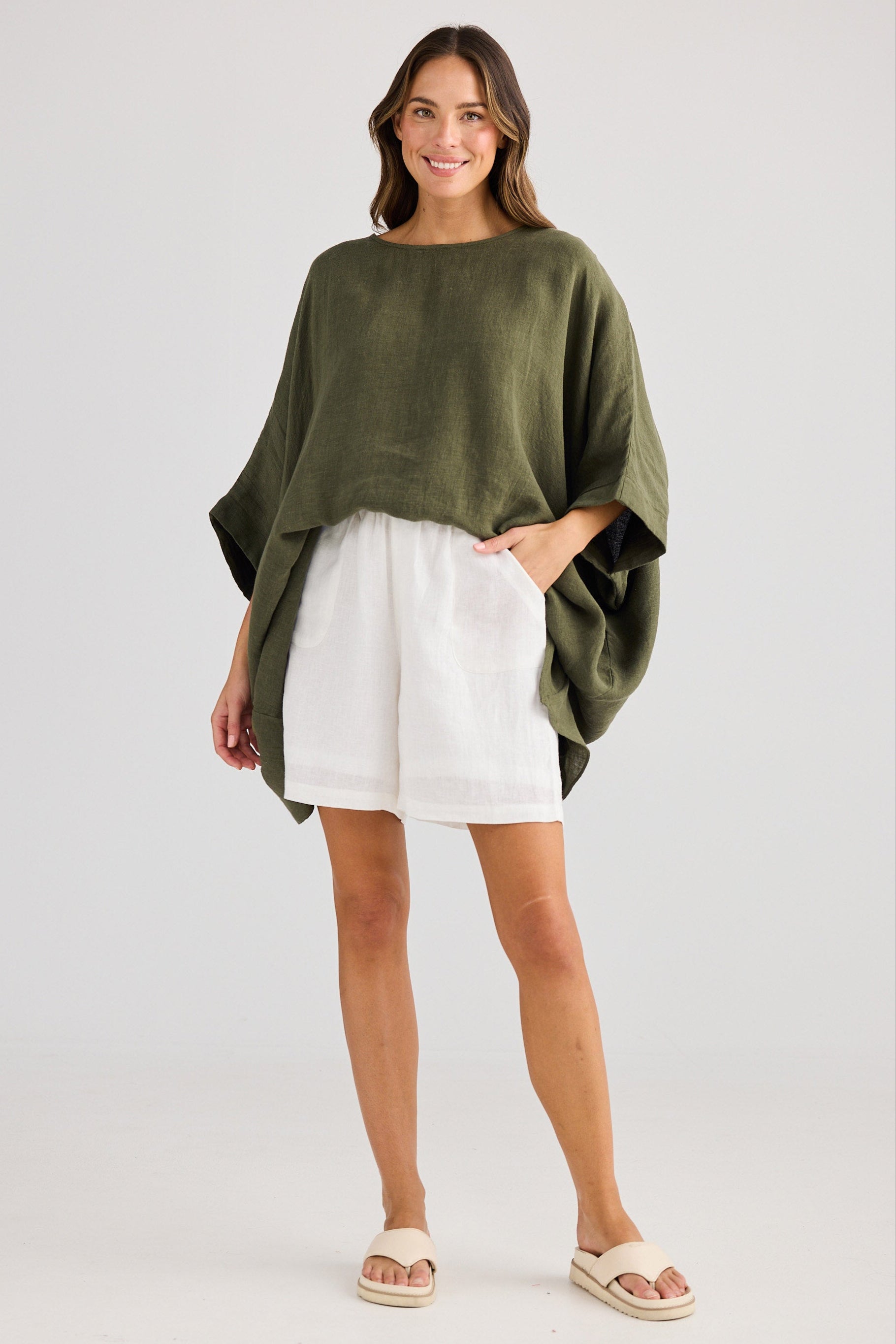 Woman wearing a green oversized sweater and white shorts on a plain background