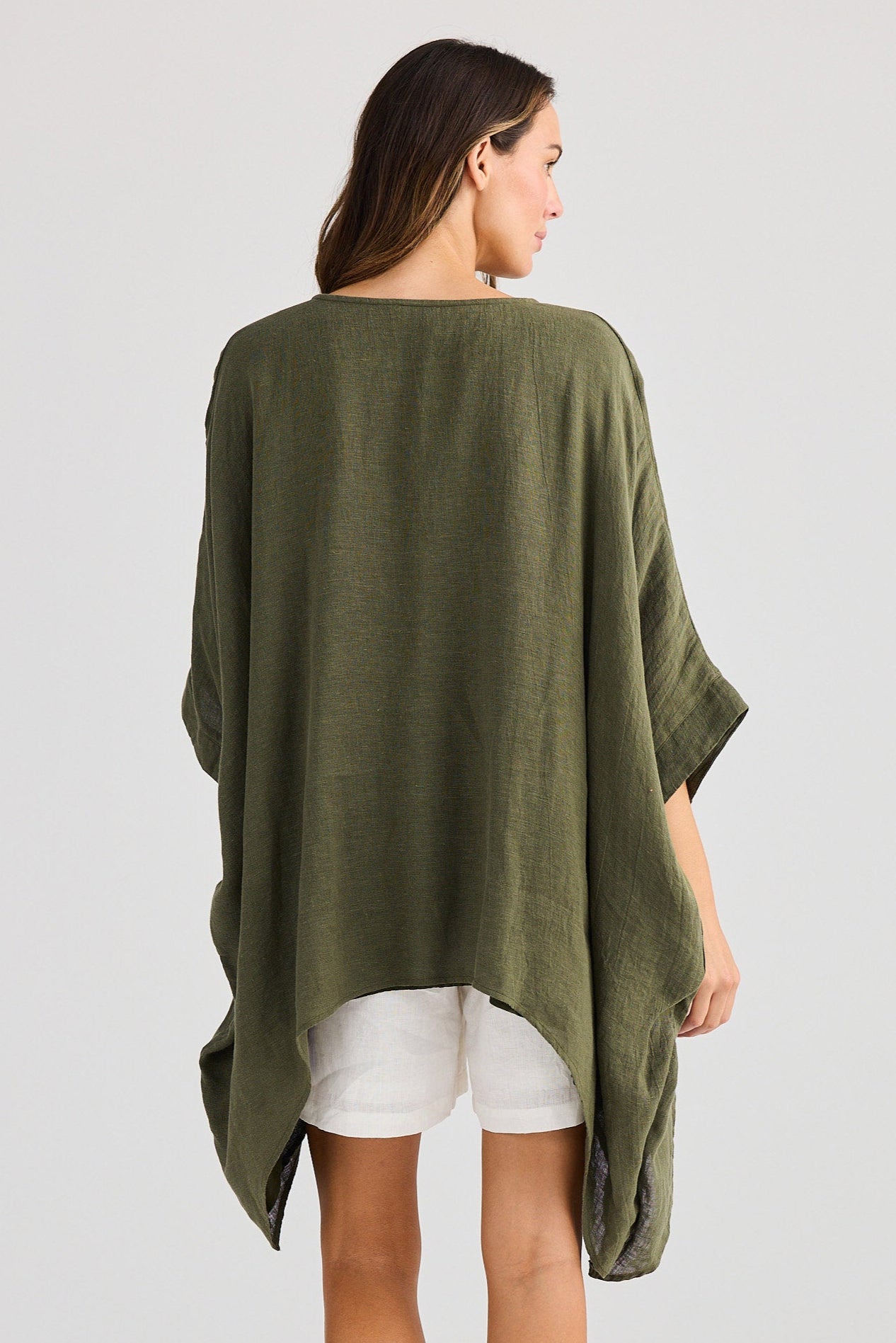 Woman wearing an olive green poncho over a white dress on a plain background