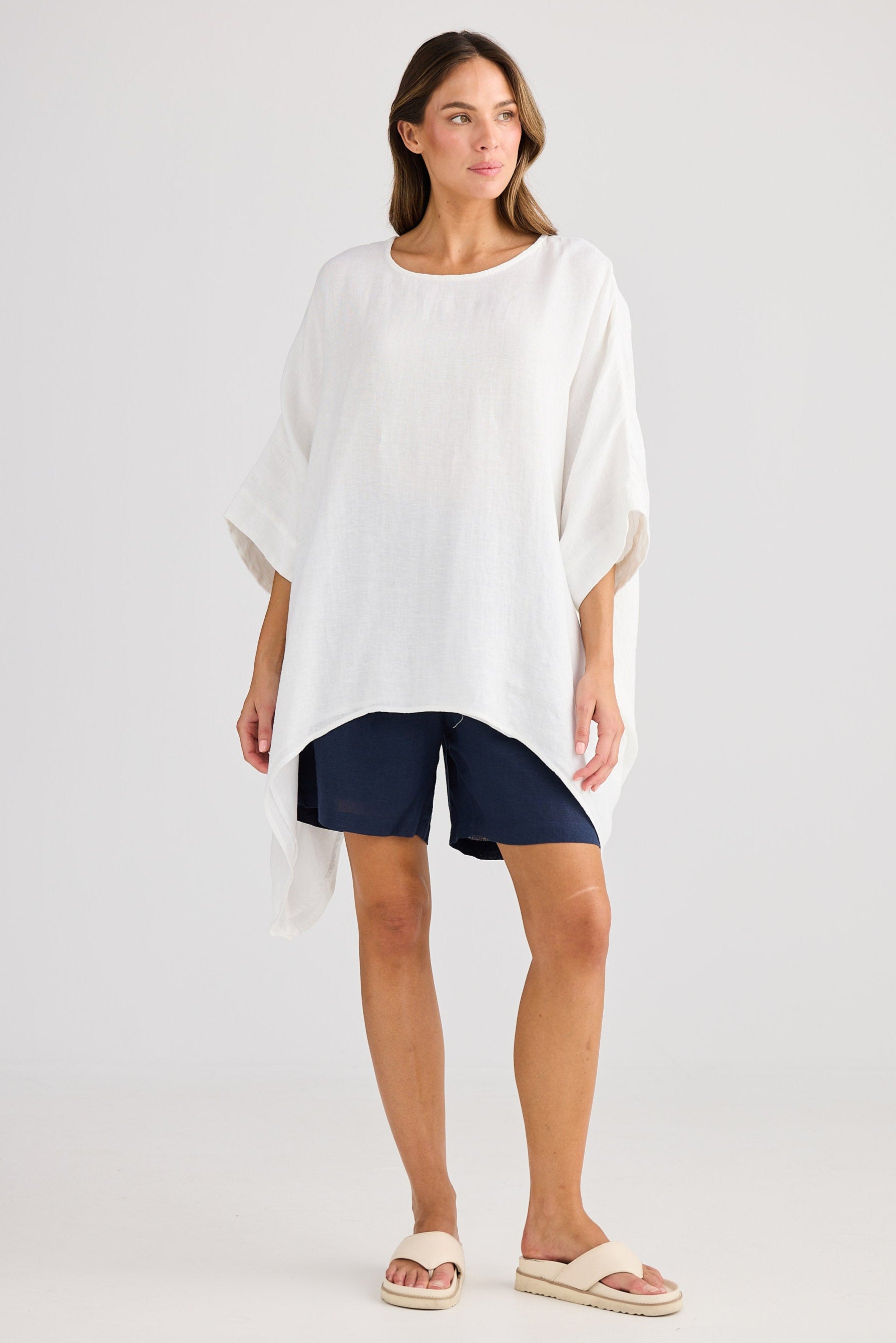 Woman wearing a white poncho over navy shorts on a plain background