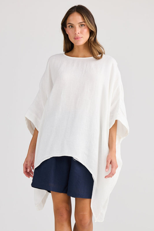 Woman wearing a white poncho over a navy dress on a light gray background