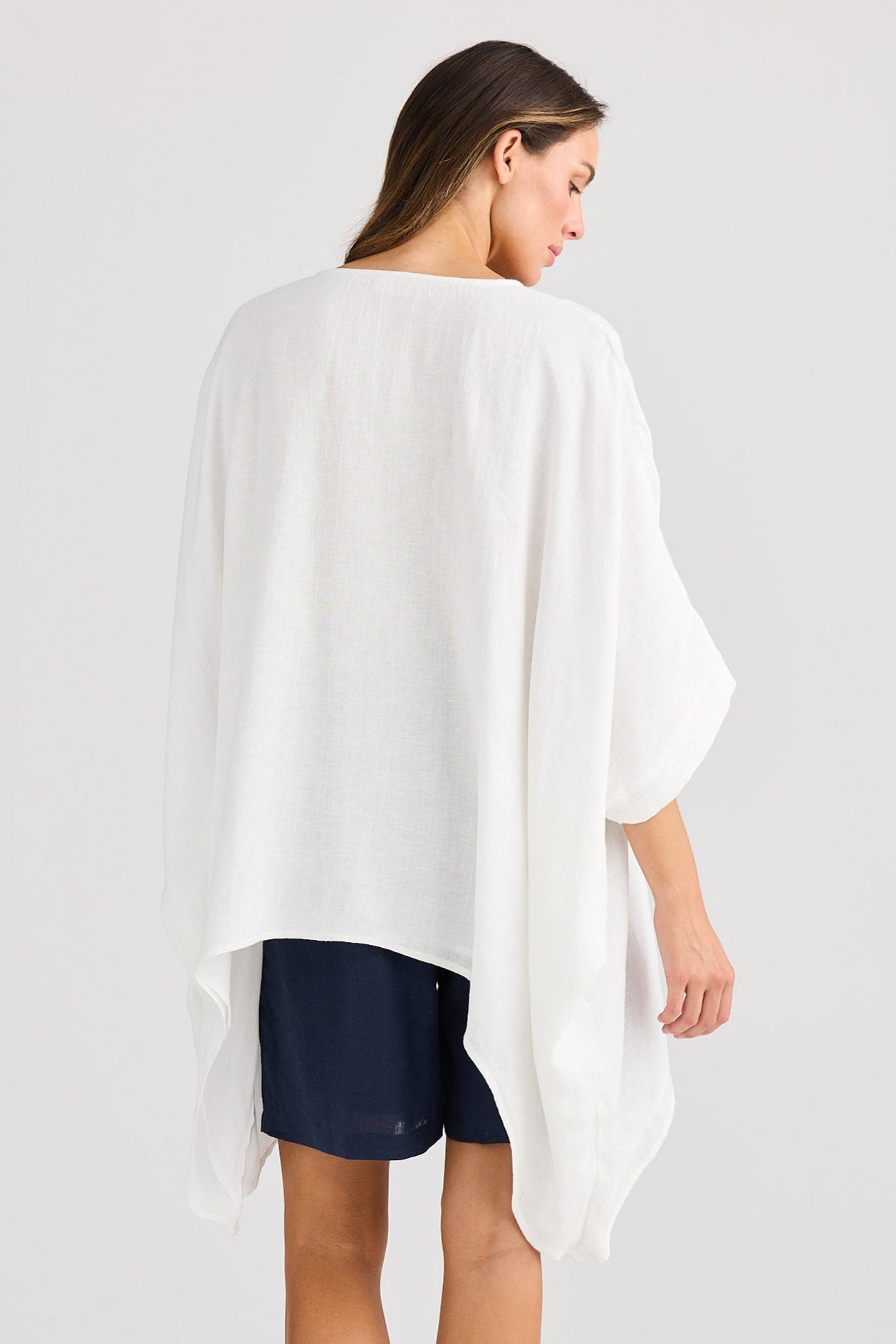 Woman wearing a white poncho over a navy dress on a light gray background