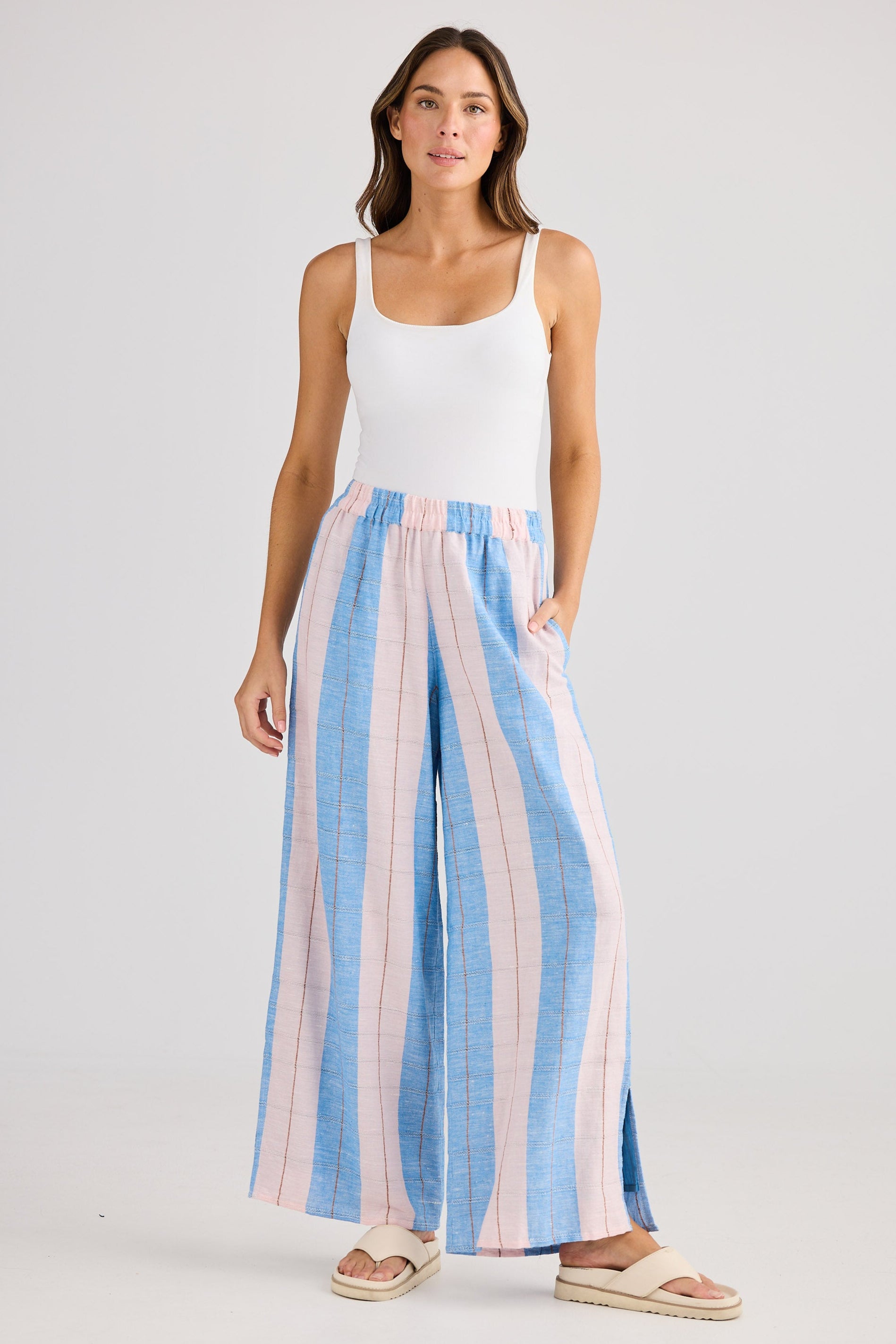 Woman wearing a white tank top and striped wide-leg pants on a plain background