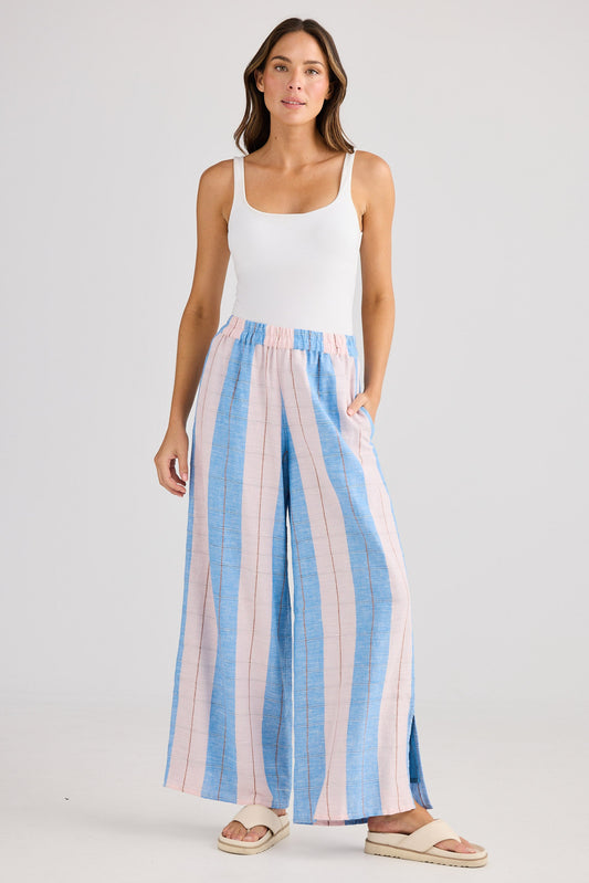 Woman wearing a white tank top and striped wide-leg pants on a plain background