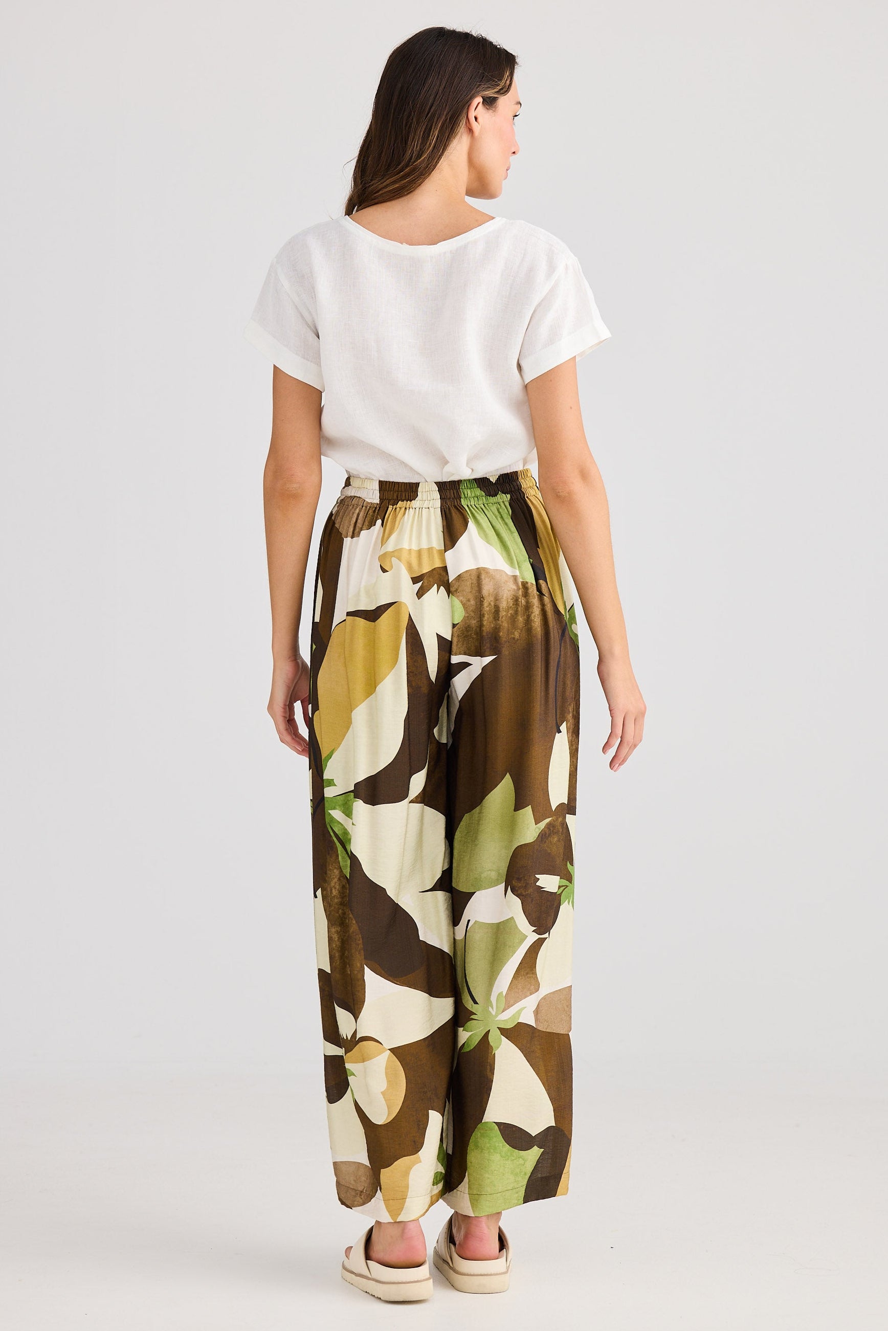 Woman wearing a white top and patterned pants on a plain background