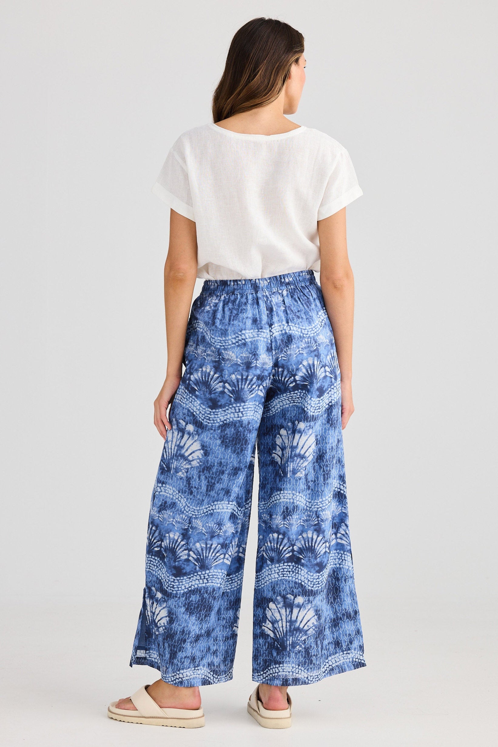Woman wearing blue floral pants and a white top on a plain background
