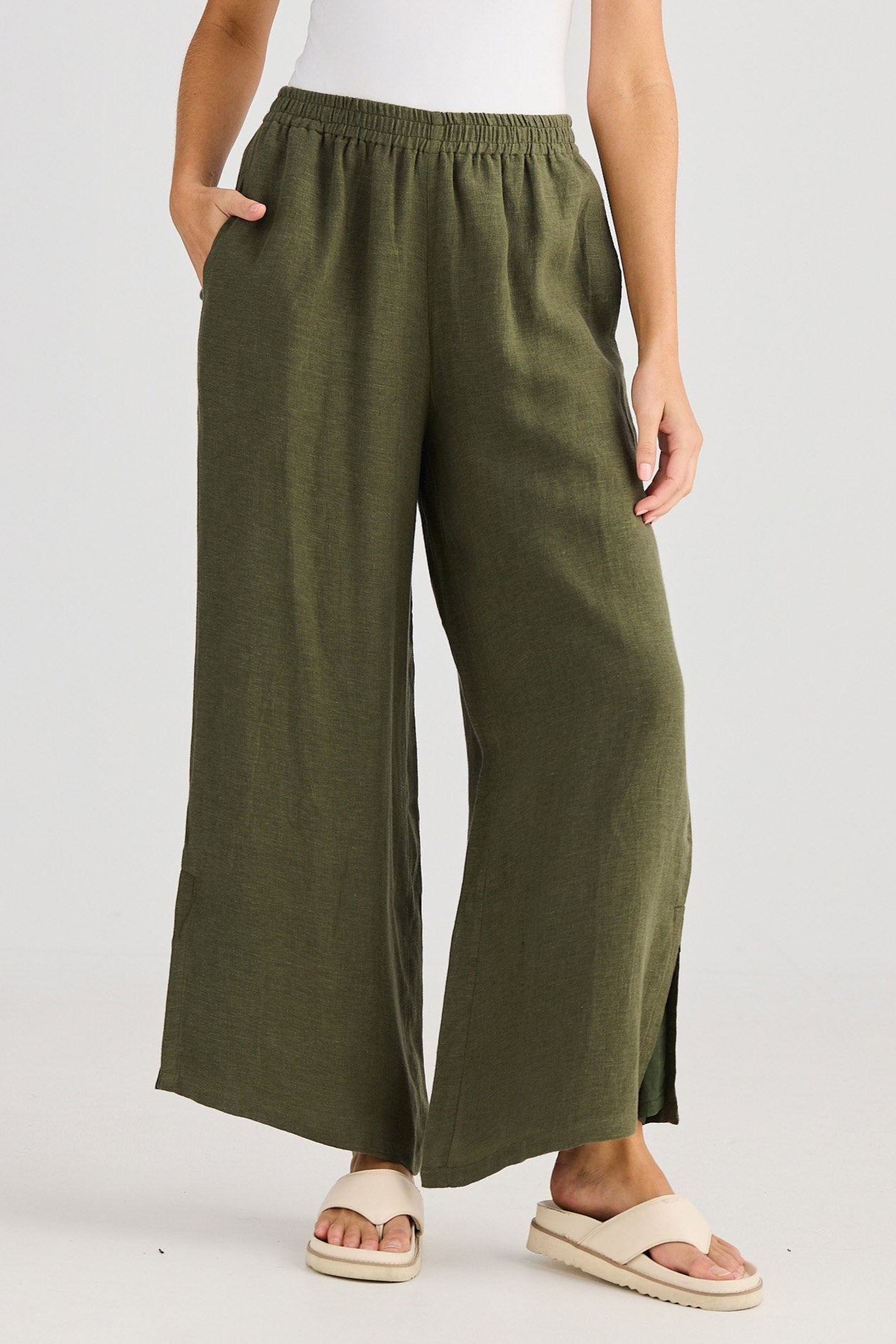 Woman wearing a white tank top and green wide-leg pants on a plain background