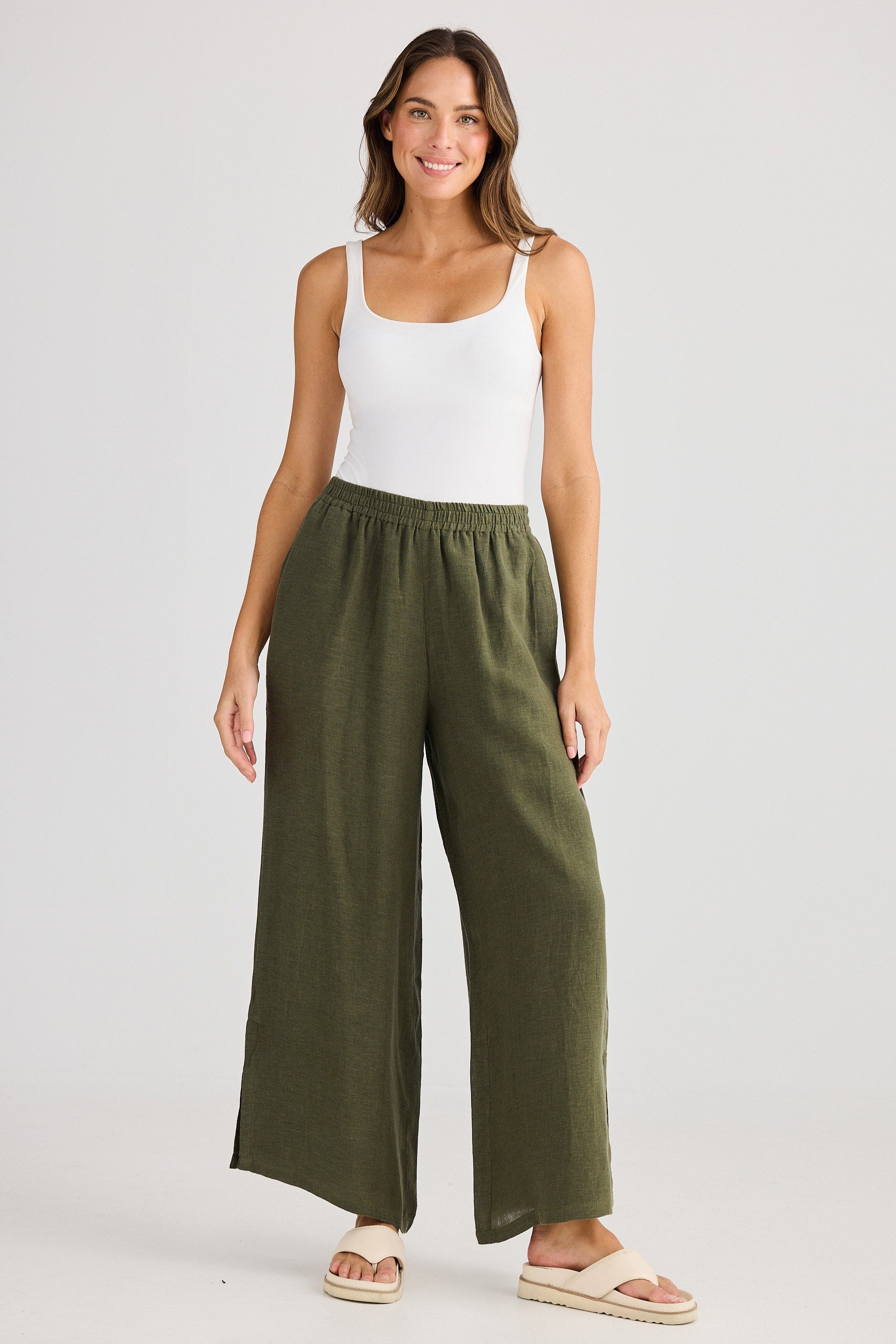 Woman wearing a white tank top and green wide-leg pants on a plain background