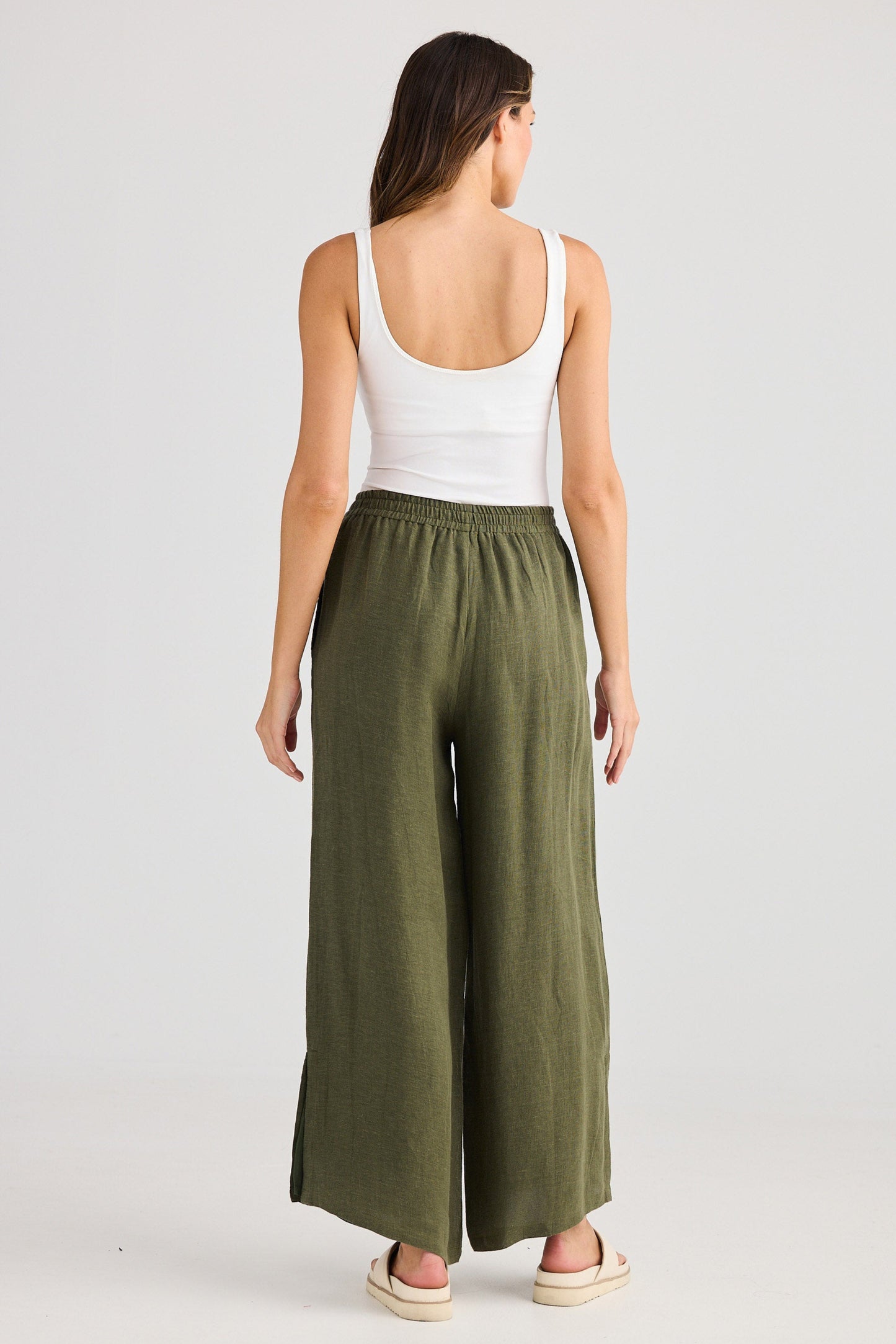 Woman wearing a white tank top and green wide-leg pants on a plain background
