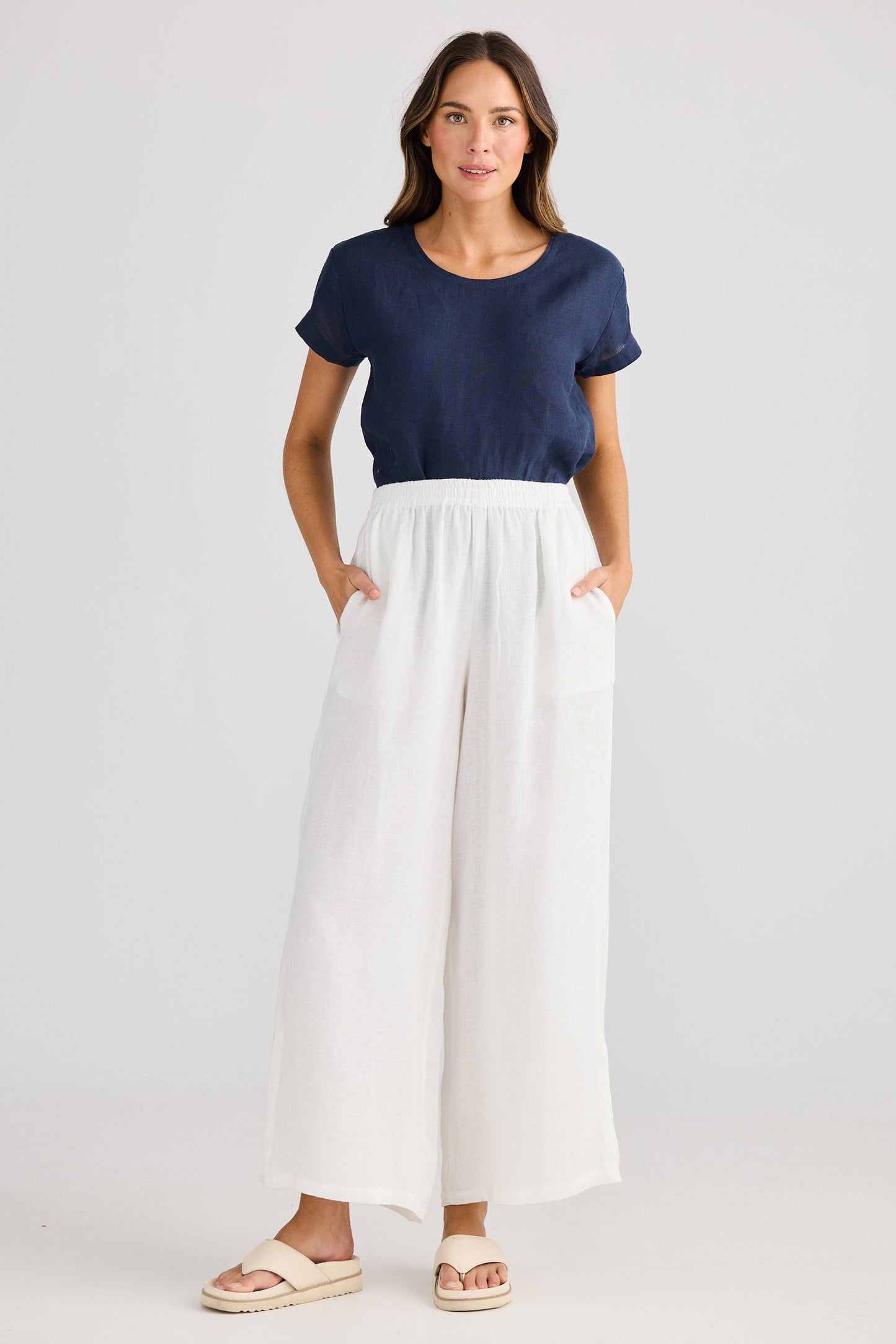 Woman wearing a navy top and white pants on a plain background