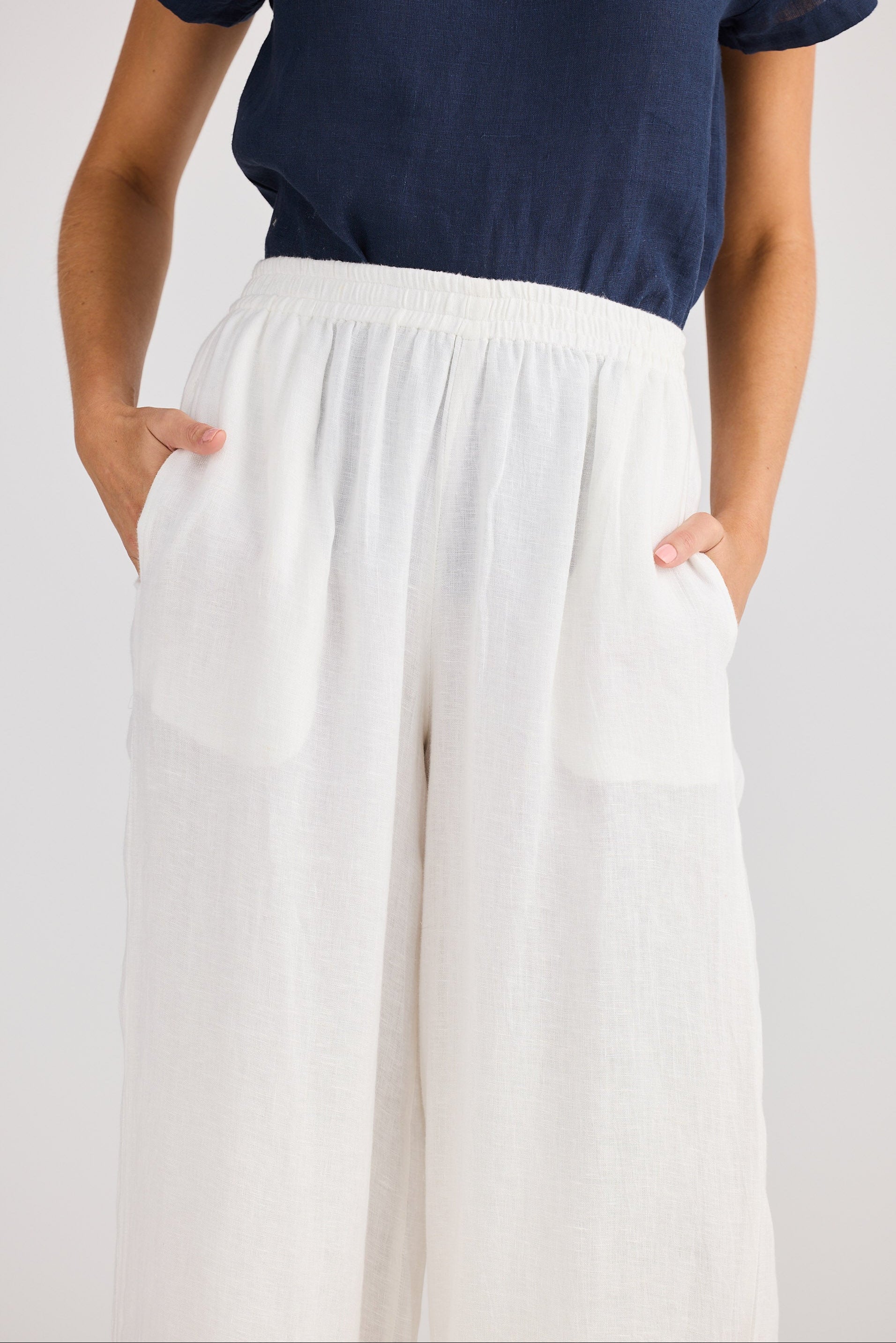 Person wearing a navy top and white pants on a plain background